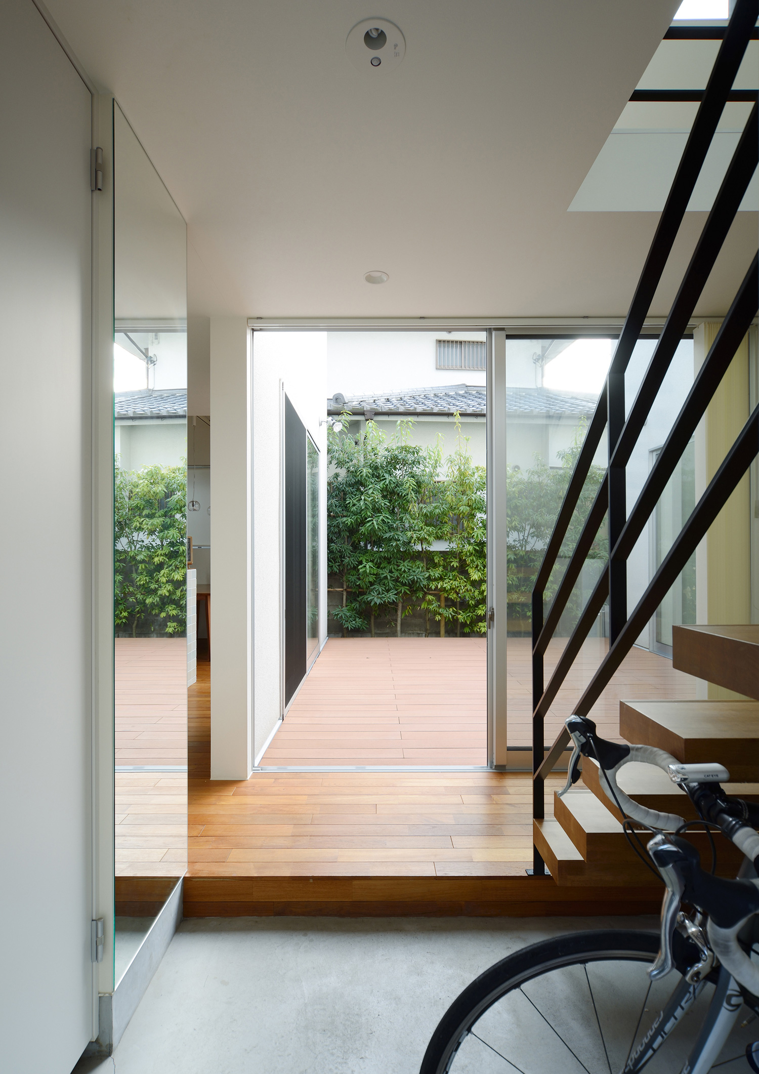 正面にウッドデッキの中庭がある明るいモルタルの玄関・デザイン住宅