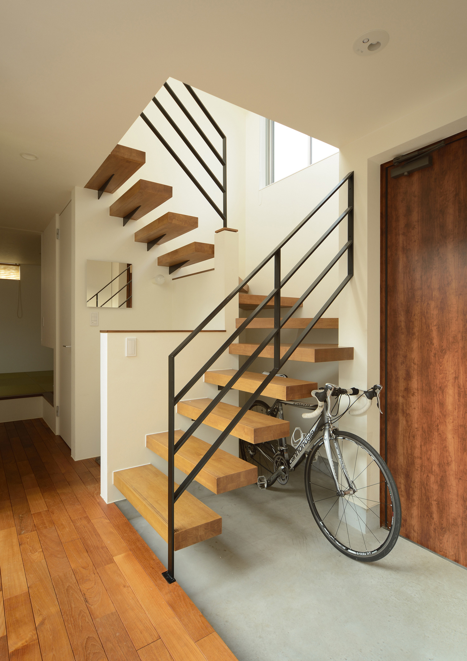 スケルトン階段の下に自転車を置いたモルタルの玄関・デザイン住宅