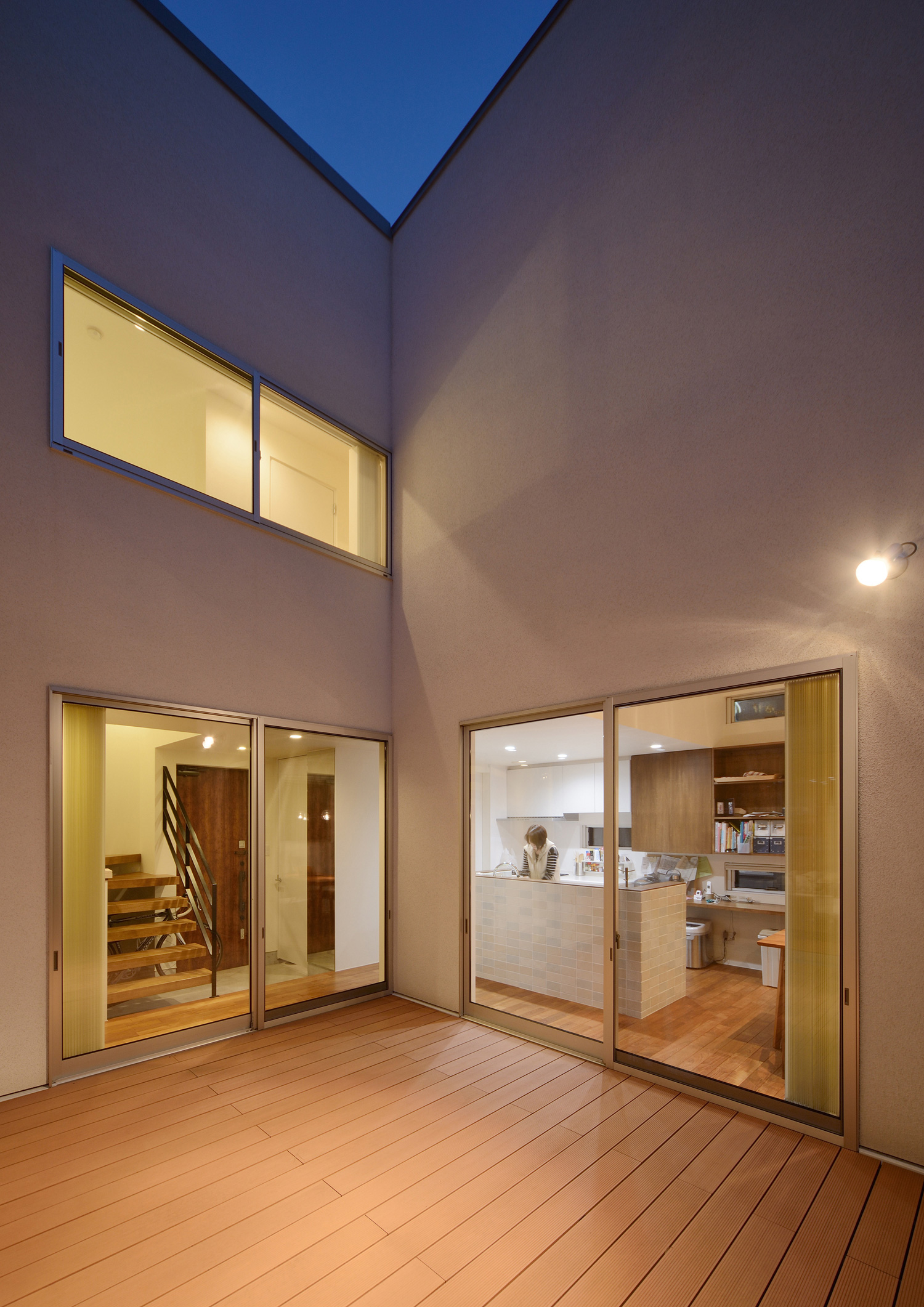 壁に照明が取り付けられたウッドデッキのプライベートな中庭・デザイン住宅