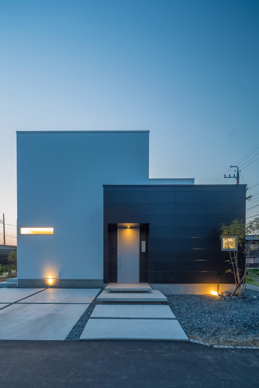 照明にライトアップされたコンクリートのアプローチがあるモノトーンの外壁の住まい・デザイン住宅