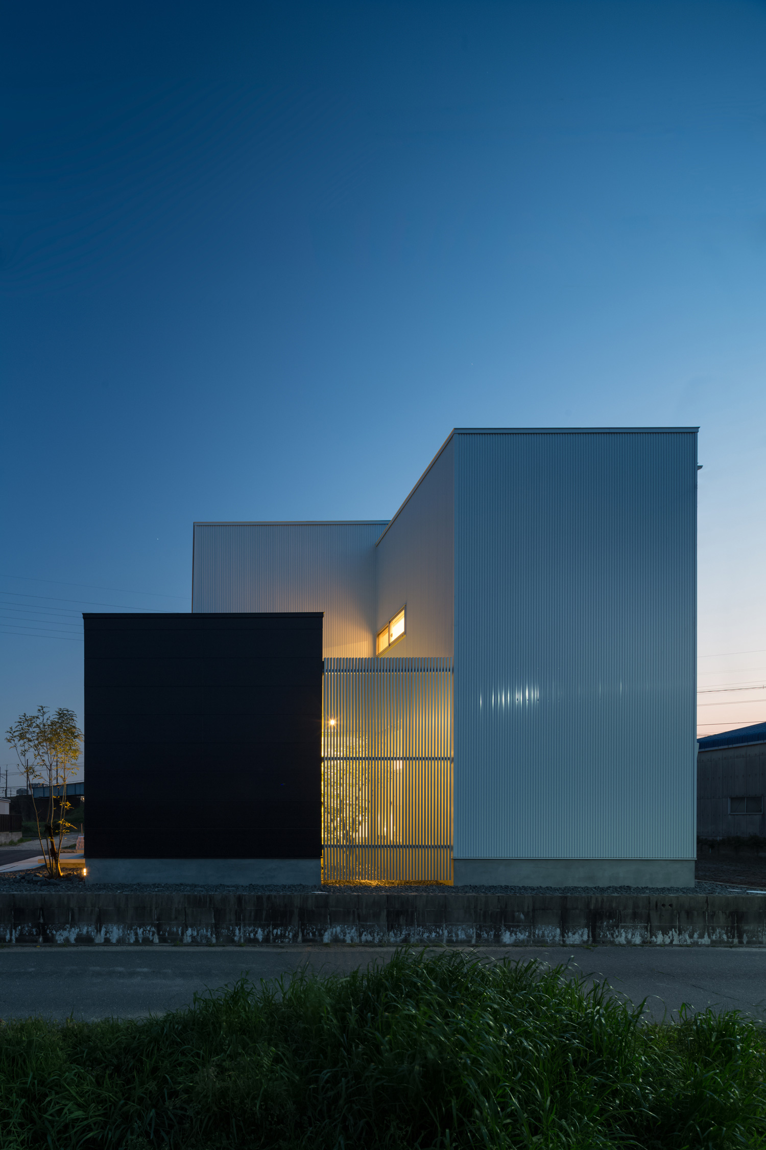 シルバーのルーバーから光が漏れるシンプルな外観の家・デザイン住宅