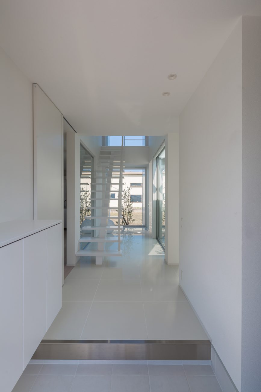 正面に窓とスケルトン階段がある白い玄関・デザイン住宅