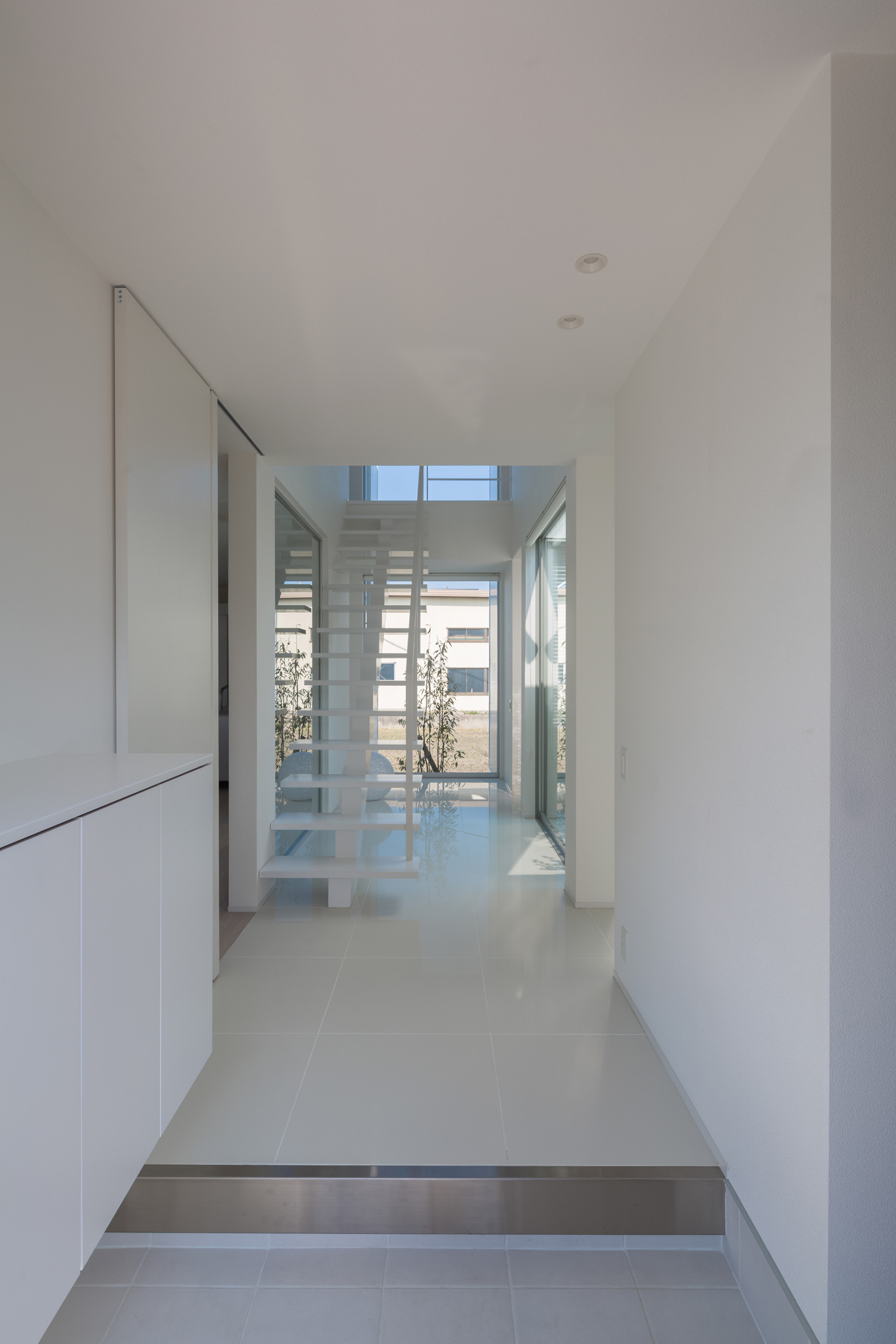 正面に窓とスケルトン階段がある白い玄関・デザイン住宅