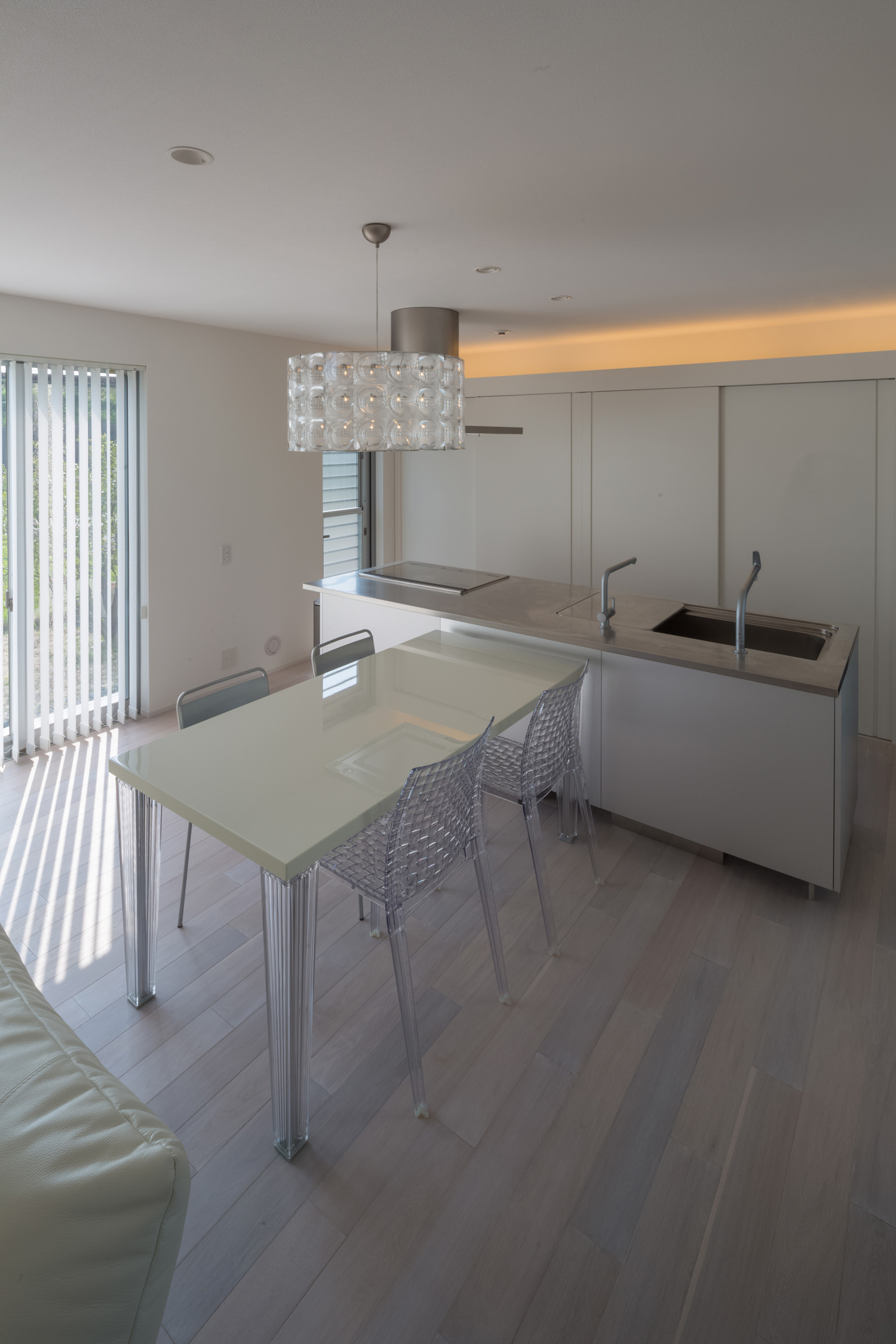 キッチンに垂直に白いダイニングテーブルが置かれたシンプルなLDK・デザイン住宅