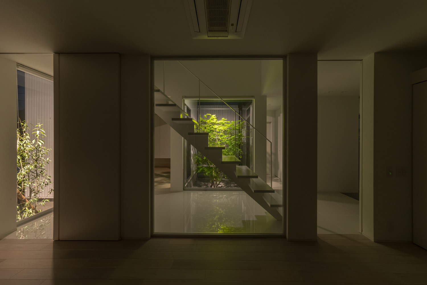 階段越しにライトアップされた植栽が見えるシンプルな廊下・デザイン住宅