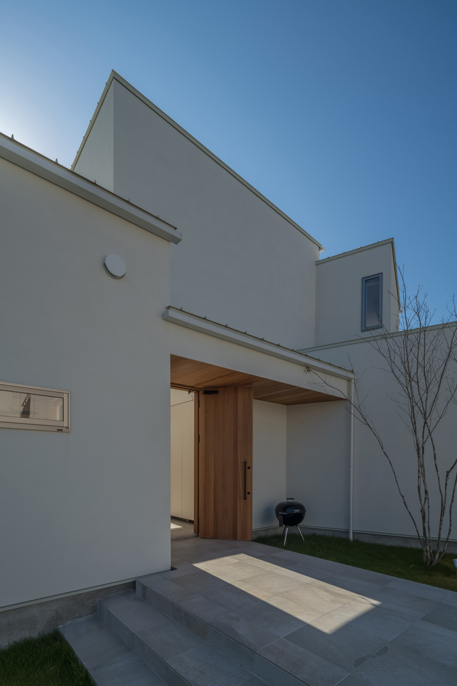 白い外壁に木の玄関扉と木の軒天井が取り付けられたアプローチ・デザイン住宅 注文住宅・デザイン住宅建築実例_『CASE495 舞台の家』_玄関