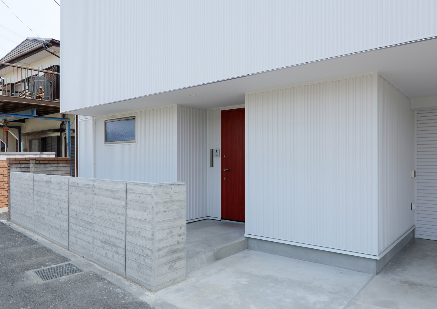 白い外壁に赤い木製の玄関扉が取り付けられた外観・デザイン住宅 注文住宅・デザイン住宅建築実例_『CASE498 シロイイエ』_外観