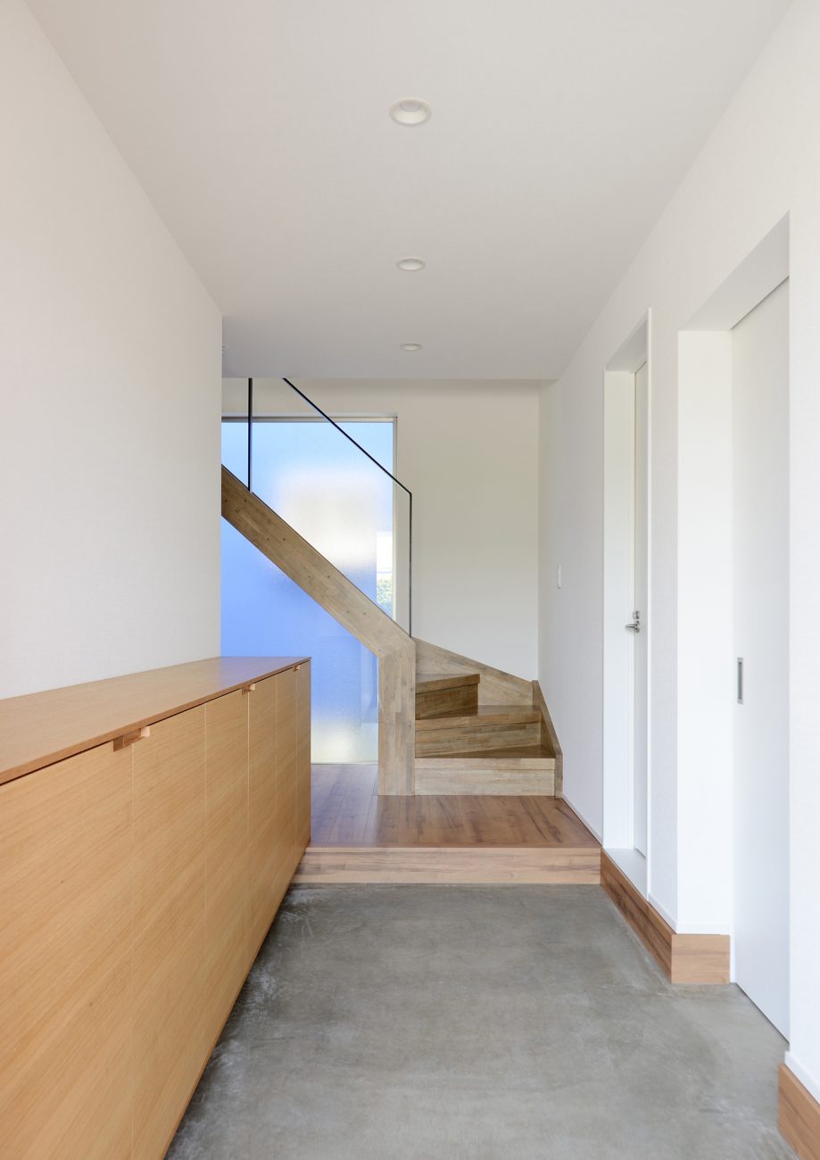 正面にスケルトン階段と大きな窓があるモルタルのシンプルな玄関・デザイン住宅 注文住宅・デザイン住宅建築実例_『CASE498 シロイイエ』_玄関