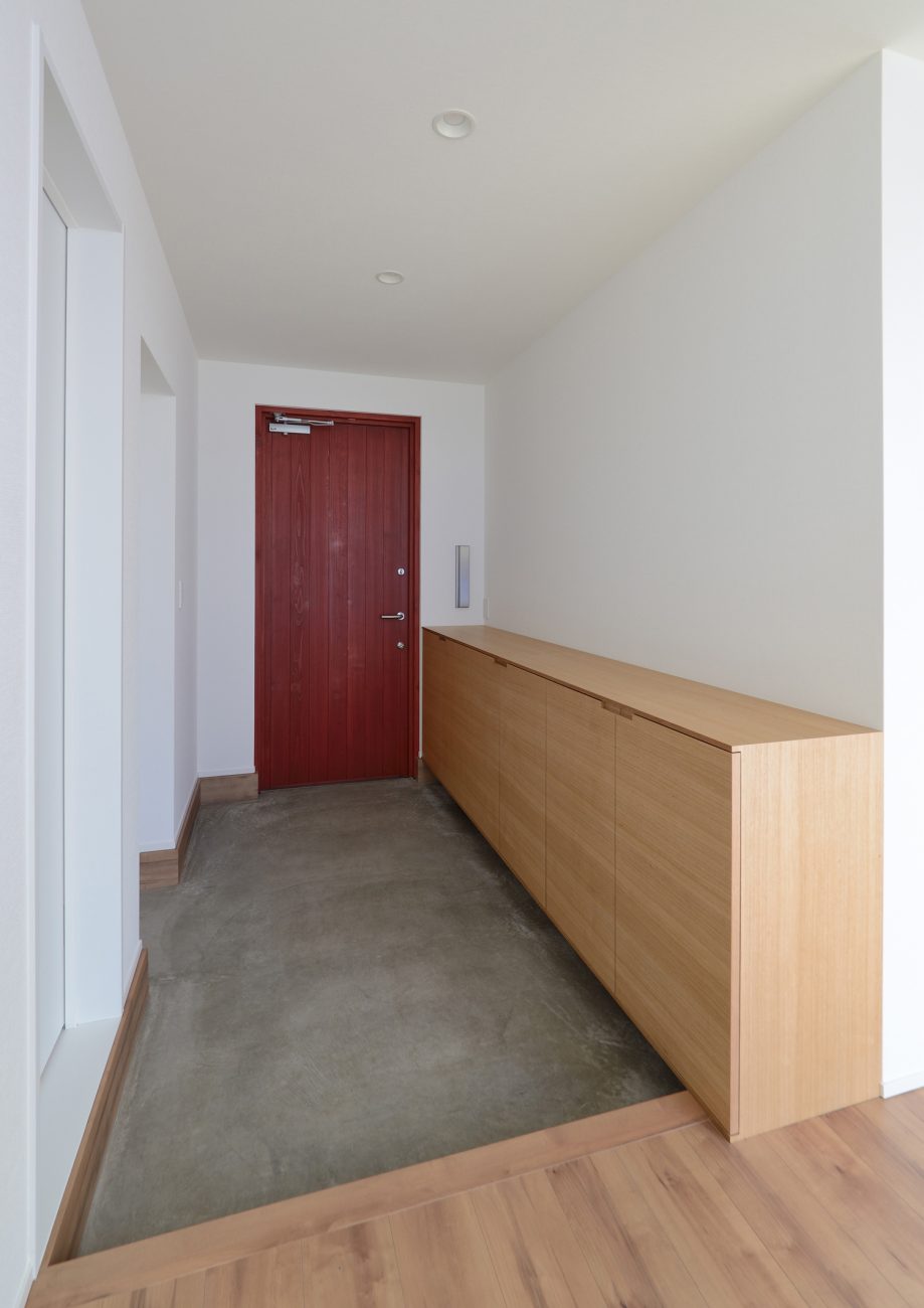 赤い玄関扉や、木のシューズボックスがあるモルタルの玄関・デザイン住宅 注文住宅・デザイン住宅建築実例_『CASE498 シロイイエ』_玄関
