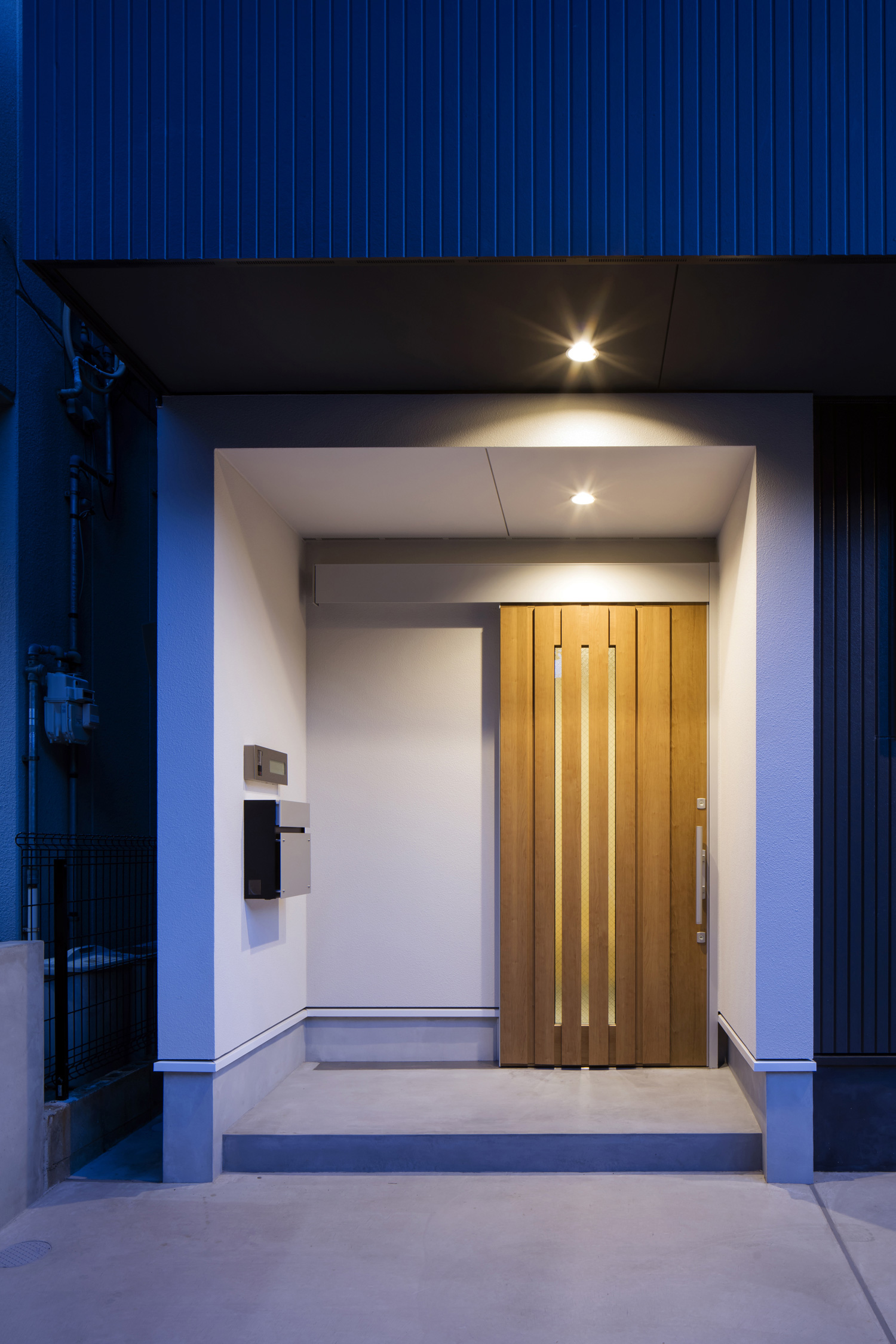 軒天井に照明が取り付けられた、木の玄関扉が取り付けられた玄関ポーチ・デザイン住宅 注文住宅・デザイン住宅建築実例_『CASE512 a　c　r　o　s　s』_外観