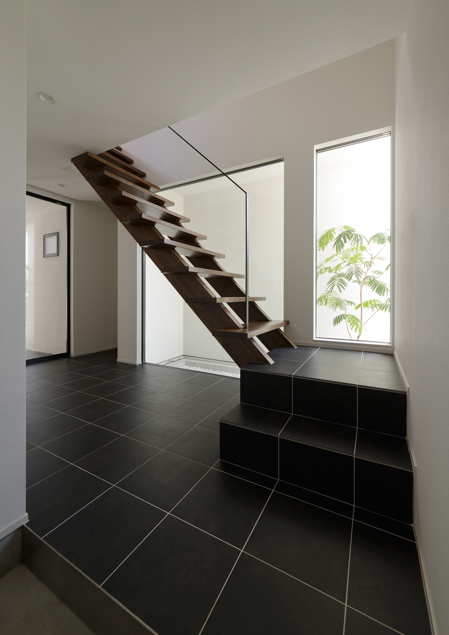正面に植栽が見える窓やスケルトン階段がある黒いタイルの玄関・デザイン住宅 注文住宅・デザイン住宅建築実例_『CASE514 Slanting Hat』_玄関