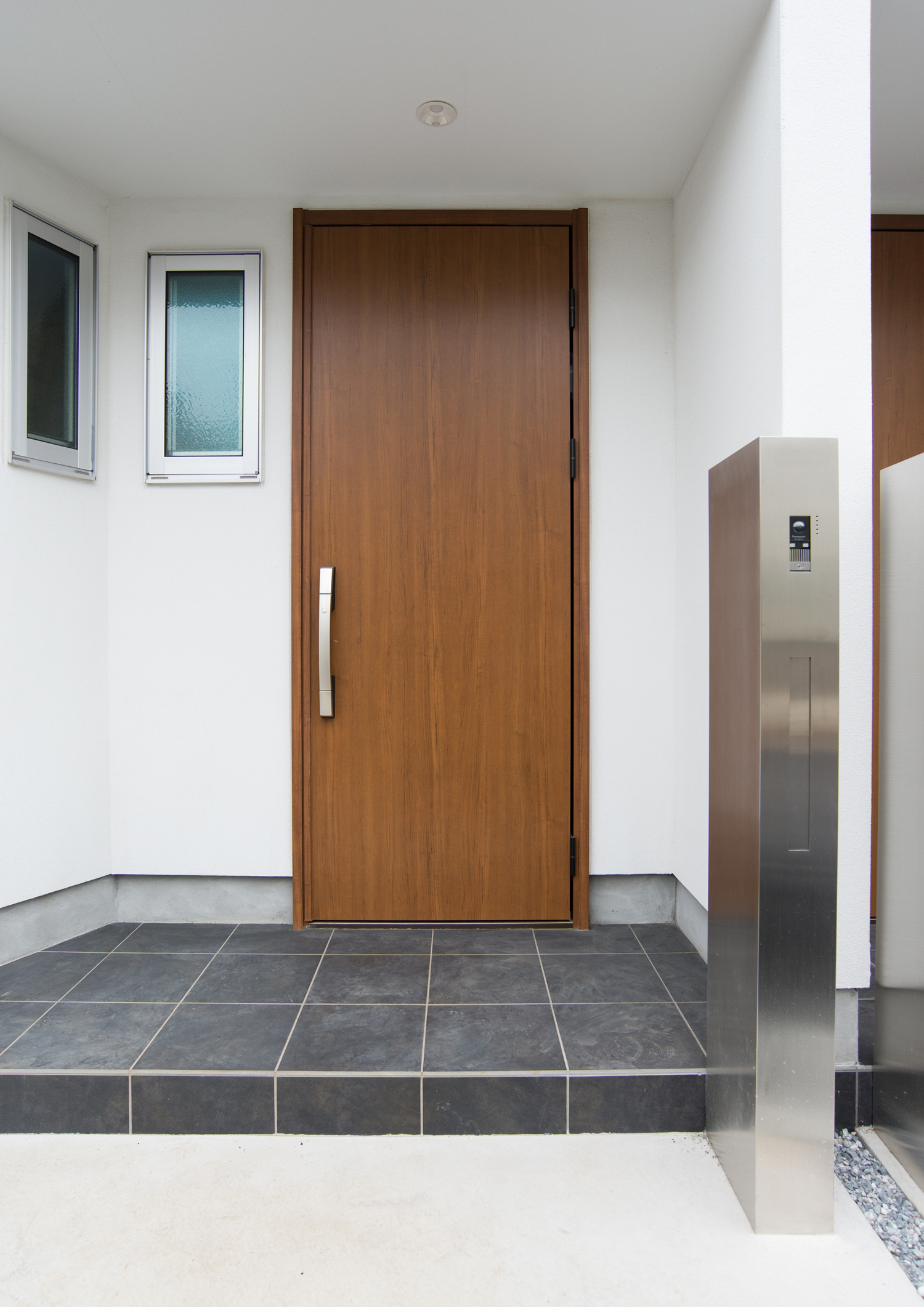 白い外壁に木の玄関扉を取り付けたシンプルな玄関・デザイン住宅 注文住宅・デザイン住宅建築実例_『CASE523 くのじのいえ』_外観