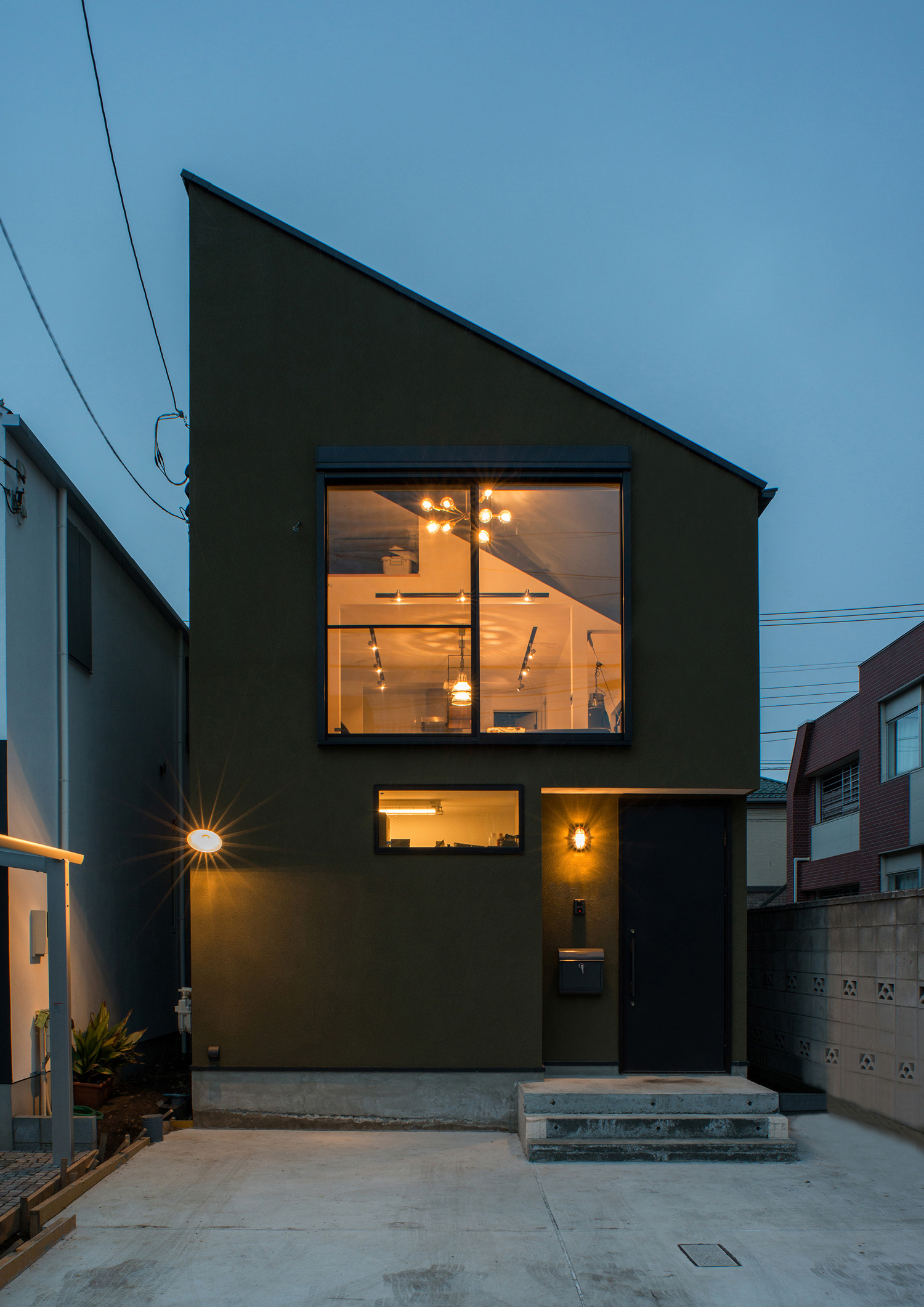 壁に照明が取り付けられ、窓から室内の光が漏れる斜め屋根の家・デザイン住宅 注文住宅・デザイン住宅建築実例_『CASE531 素地』_外観