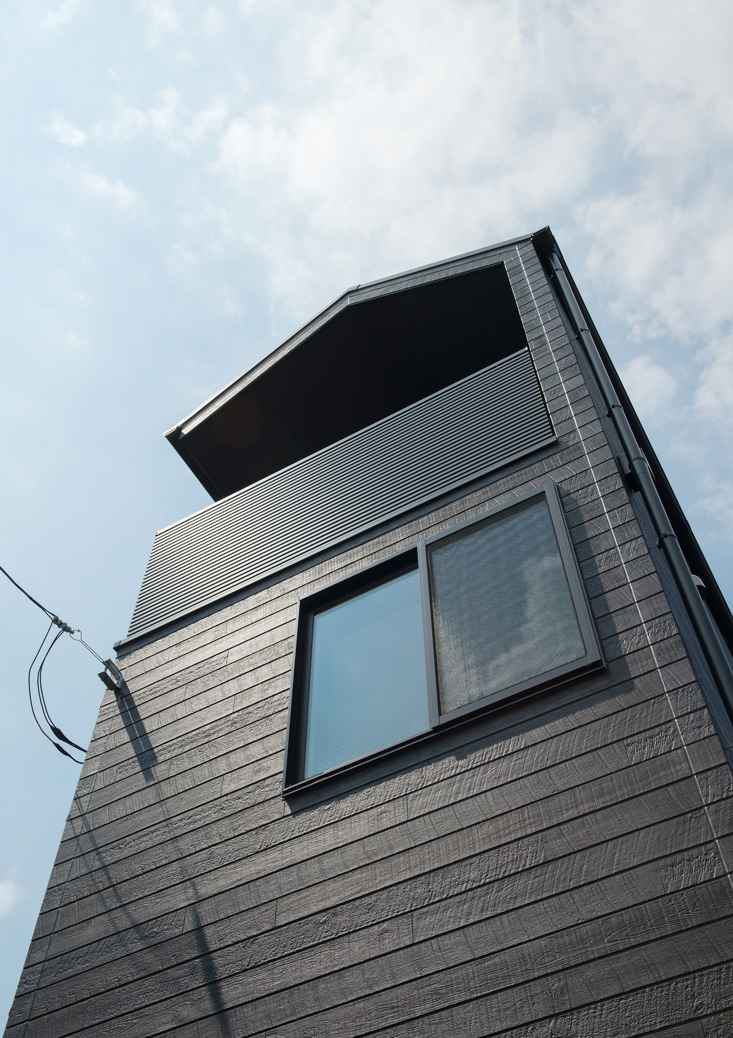 窓やバルコニーがあるダークブラウンの外壁の家を見上げた様子・デザイン住宅 注文住宅・デザイン住宅建築実例_『CASE562 タテ長い家』_外観