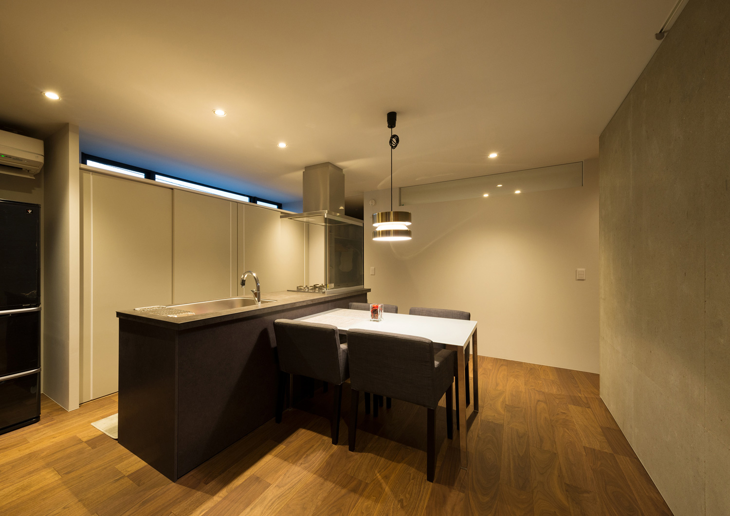 黒いアイランドキッチンの前にあるペンダントライトに照らされた四人掛けのダイニングテーブル・デザイン住宅 注文住宅・デザイン住宅建築実例_『CASE573 次代の家』_キッチン