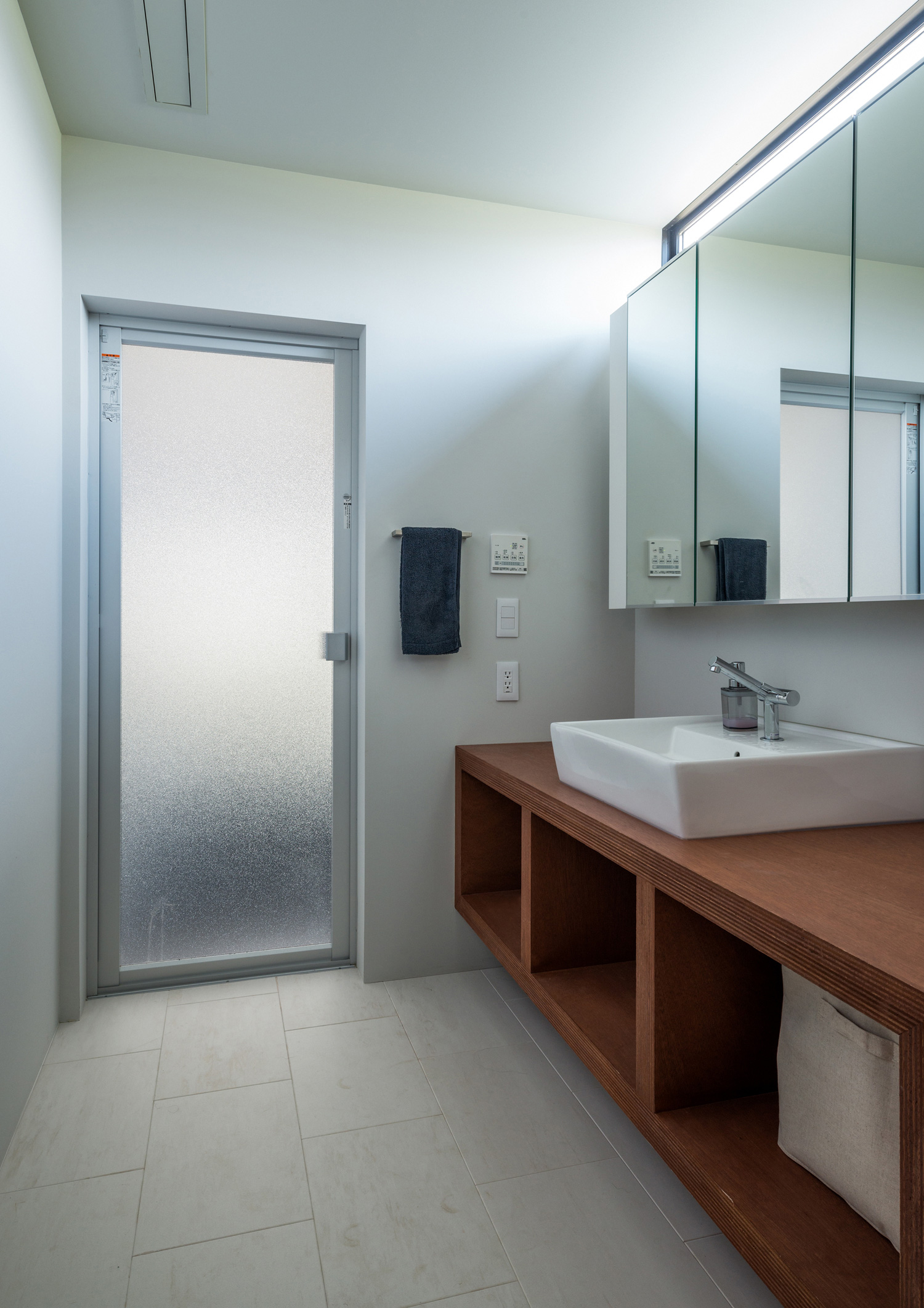 鏡の上にスリット窓を設けた洗面台と、浴室に繋がる曇りガラスのドア・デザイン住宅 注文住宅・デザイン住宅建築実例_『CASE573 次代の家』_浴室・洗面所