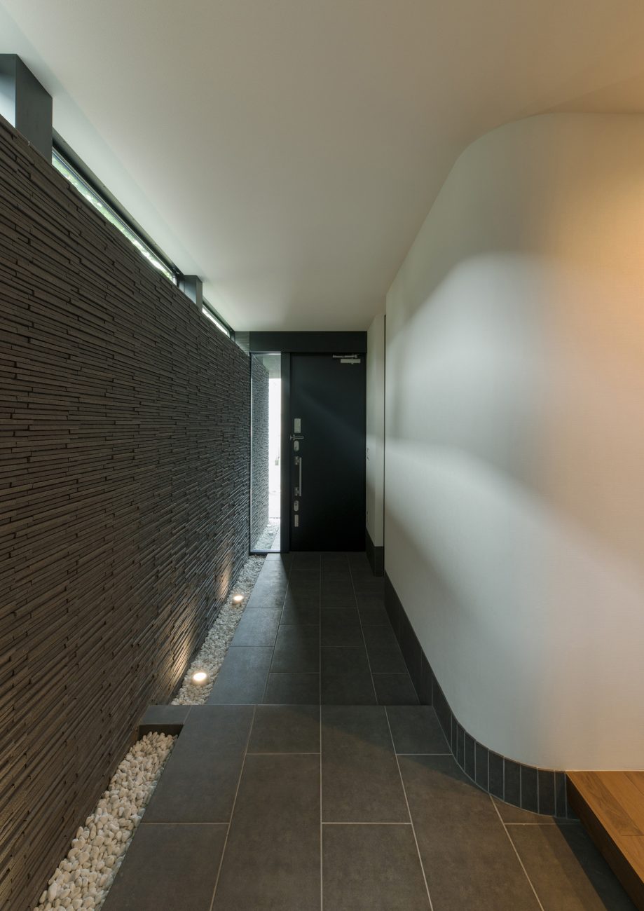 石の壁や壁際に敷石があるタイルの玄関・デザイン住宅 注文住宅・デザイン住宅建築実例_『CASE577 紬（つむぎ）の家』_玄関