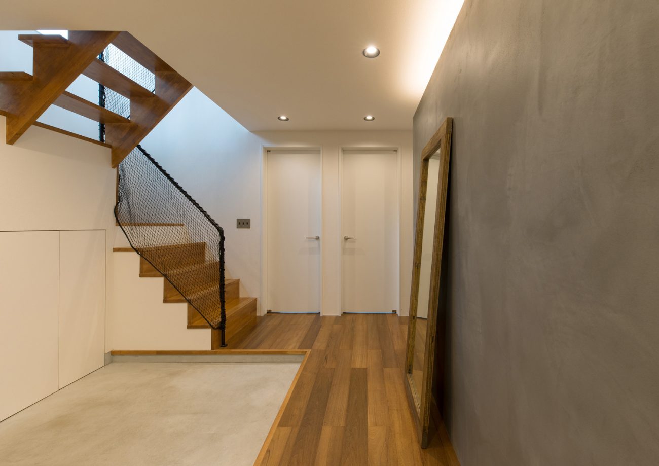 グレーのアクセントウォールの壁際に間接照明が取り付けられたフローリングの廊下・デザイン住宅 注文住宅・デザイン住宅建築実例_『CASE582 大切な時を刻む家』_玄関