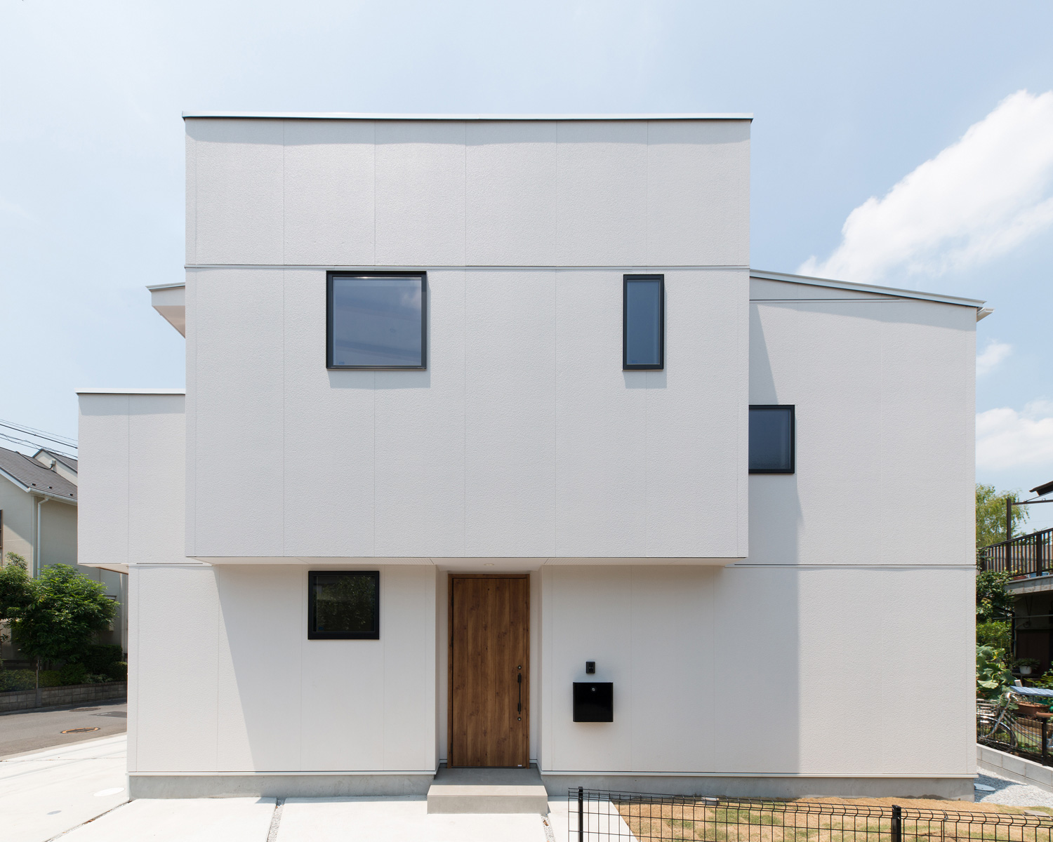 白い外壁に木の玄関扉が取り付けられている外観の家・デザイン住宅 注文住宅・デザイン住宅建築実例_『CASE586 サクラクリヒノキ』_外観