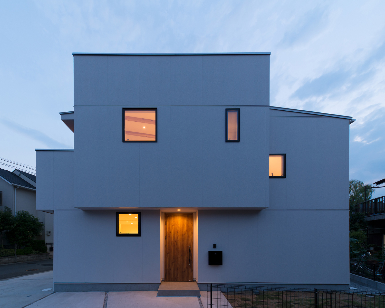 木目の玄関扉が軒天井の照明に照らされる白い外壁の家・デザイン住宅 注文住宅・デザイン住宅建築実例_『CASE586 サクラクリヒノキ』_外観