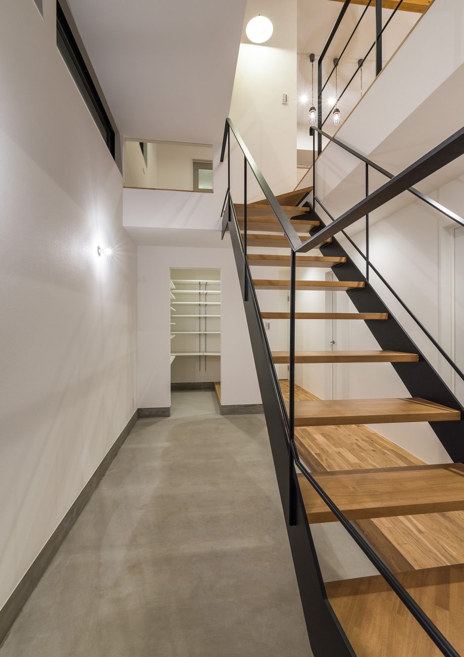 シューズインクローゼット付きのモルタルの玄関のそばにある木製のスケルトン階段・デザイン住宅 注文住宅・デザイン住宅建築実例_『CASE590 つなぐ家』_玄関