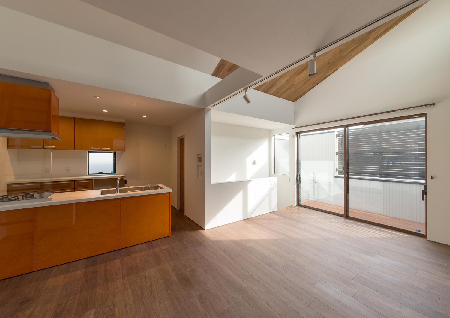 ウッドデッキのバルコニーとフラットに繋がるオレンジのキッチンがあるLDK・デザイン住宅 注文住宅・デザイン住宅建築実例_『CASE596 【edge】』_LDK