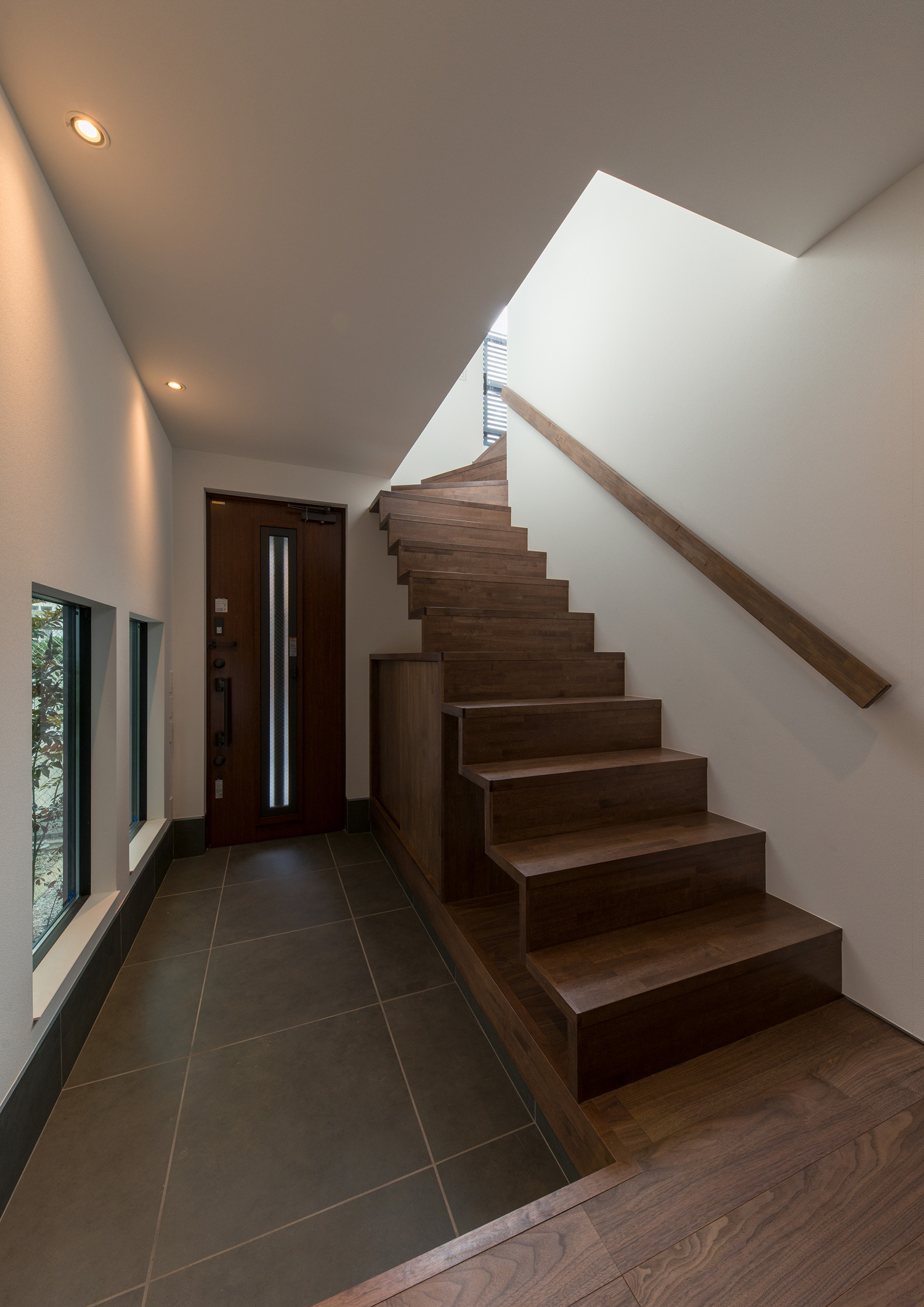 タイル貼りの玄関の隣にある木製のスケルトン階段・デザイン住宅 注文住宅・デザイン住宅建築実例_『CASE596 【edge】』_玄関