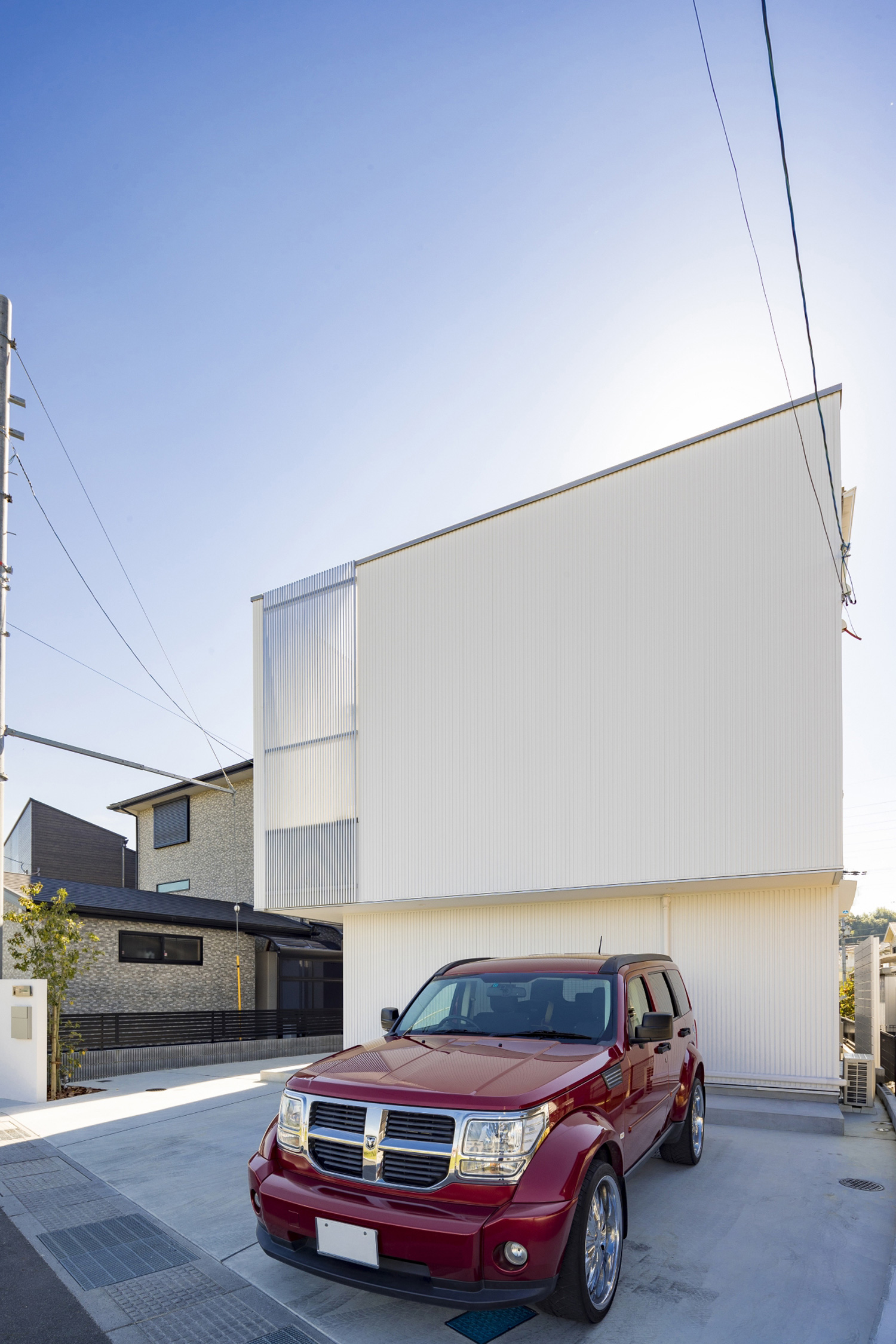 白いガルバリウム鋼板の外壁の家の前に赤い車が一台止まっている様子・デザイン住宅 注文住宅・デザイン住宅建築実例_『CASE598 爽　～風と光～』_外観
