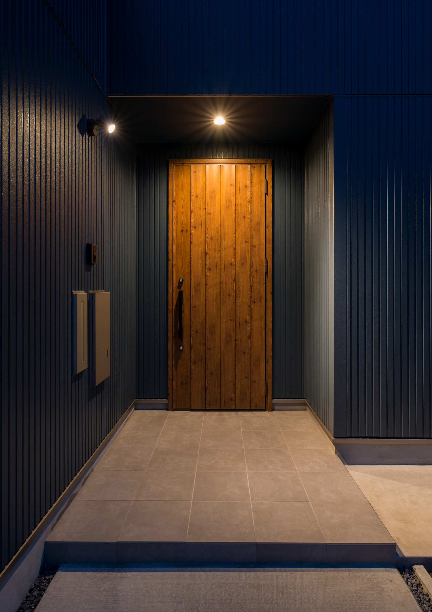 木目の玄関扉が軒天井のダウンライトに照らされる様子・デザイン住宅 注文住宅・デザイン住宅建築実例_『CASE601 ドマノイエ』_外観