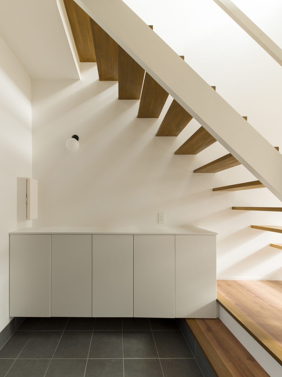 白いシューズボックスが置かれた玄関をスケルトン階段が横切る様子・デザイン住宅 注文住宅・デザイン住宅建築実例_『CASE611 黒曜×石英』_玄関