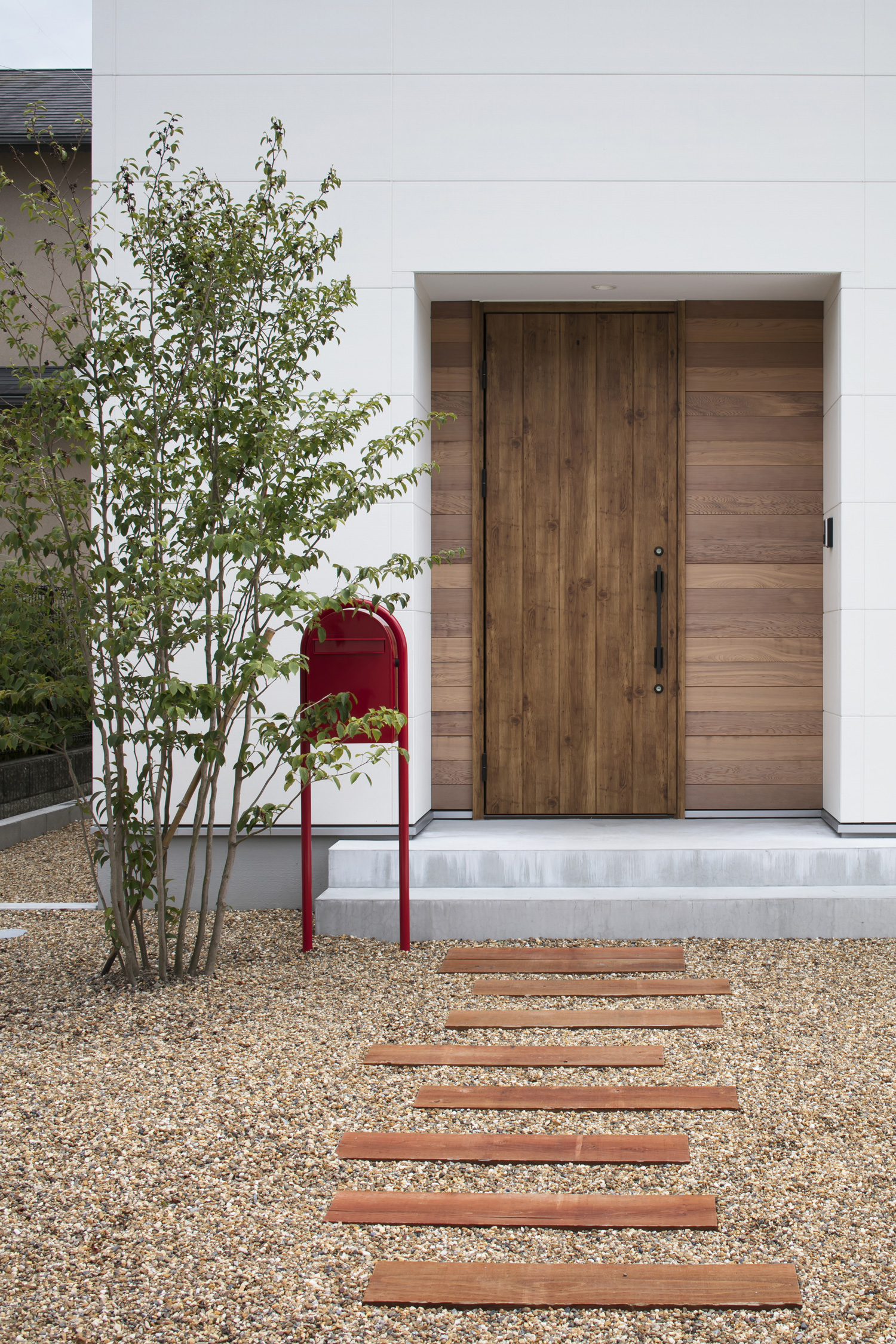 砂利と枕木で作られたアプローチの先に木の玄関扉がある住宅・デザイン住宅 注文住宅・デザイン住宅建築実例_『CASE619 Hoccori』_外観