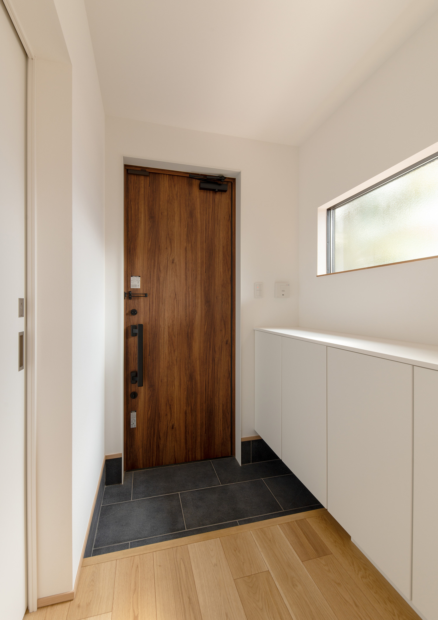 木の玄関扉で、白い壁付きのシューズボックスがある玄関・デザイン住宅 注文住宅・デザイン住宅建築実例_『CASE620 継承する家』_玄関