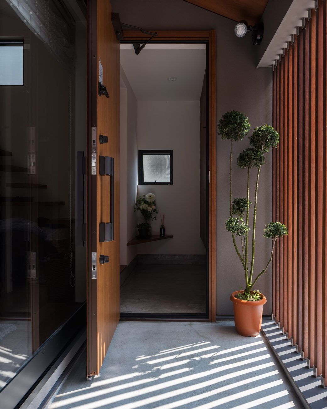 ルーバーの目隠し壁があり、観葉植物が置かれた、扉を開けた玄関・デザイン住宅 注文住宅・デザイン住宅建築実例_『CASE622 fit』_玄関