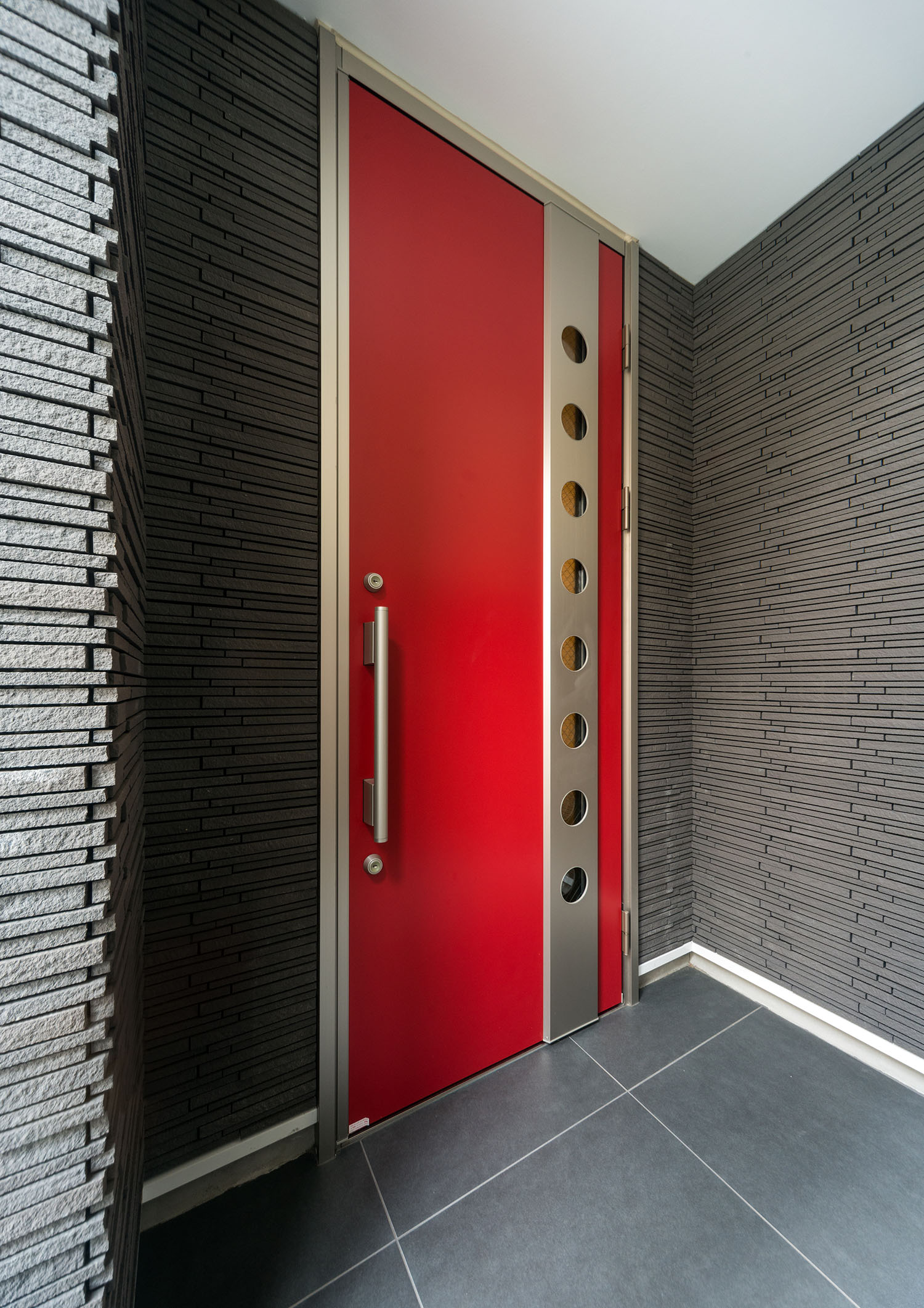 赤い玄関扉を取りつけたグレーのタイルの壁の玄関ポーチ・デザイン住宅 注文住宅・デザイン住宅建築実例_『CASE460 三色　～さんしき～』_外観