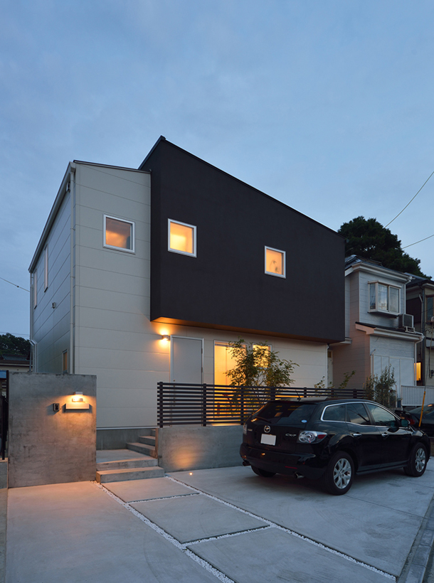 広いコンクリートの駐車スペースがあるモノトーンの外観の家・デザイン住宅