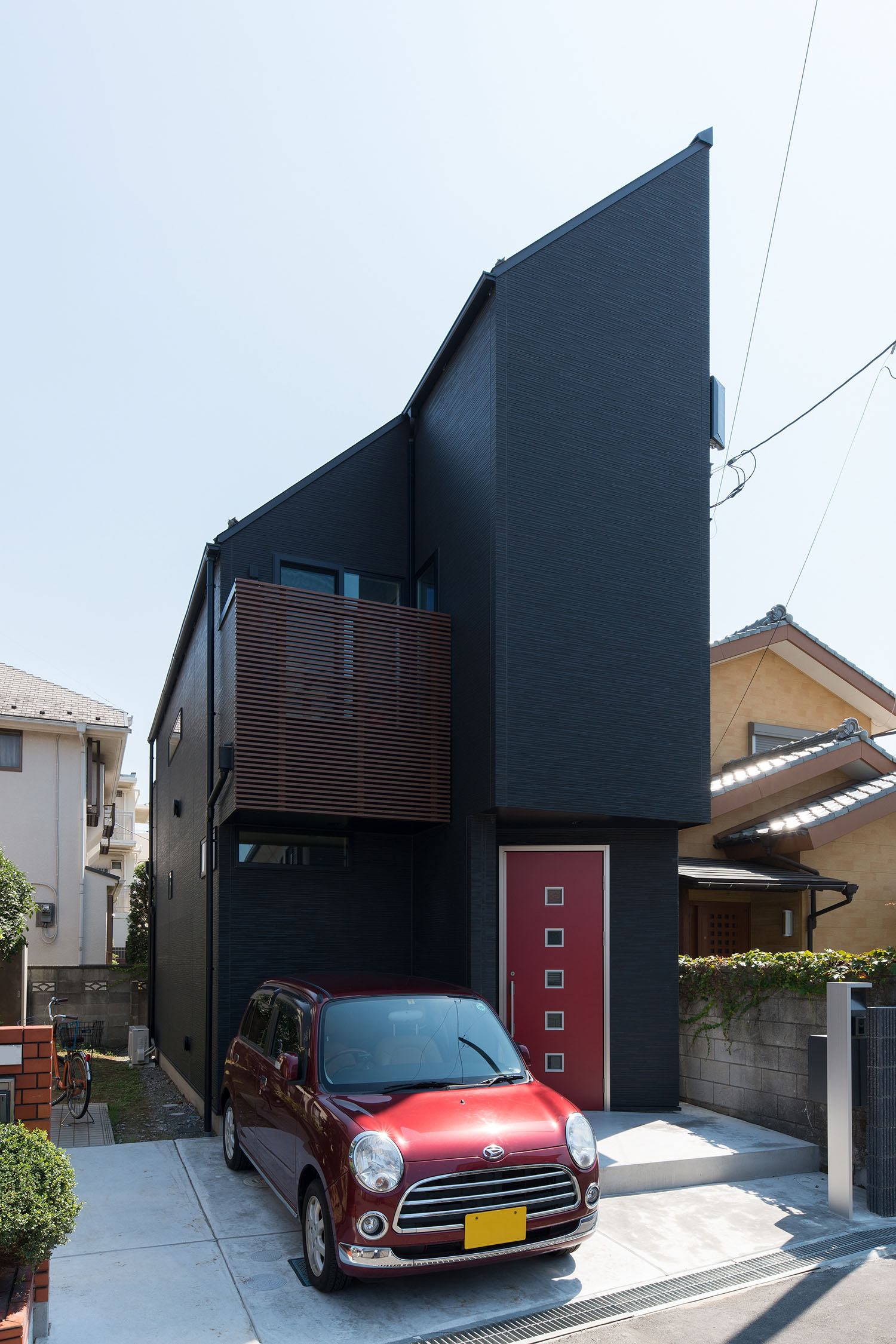 赤い玄関扉が付いた黒い斜め屋根の家の前に赤い軽自動車が一台止まっている様子・デザイン住宅 注文住宅・デザイン住宅建築実例_『CASE594 TOOL　BOX』_外観