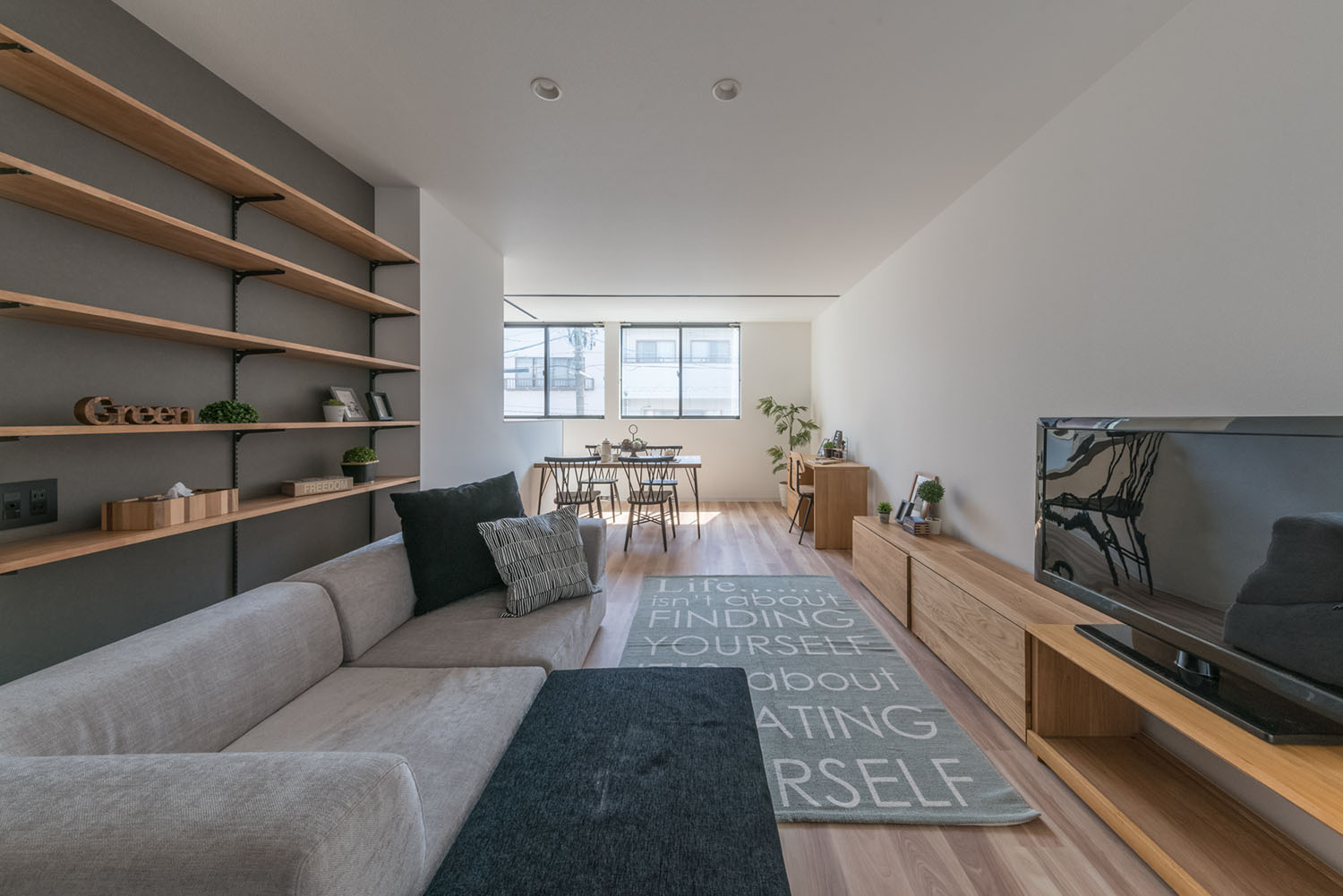 グレーのアクセントクロスに木製の可動棚が取り付けられた、L字ソファーのあるLDK・デザイン住宅 注文住宅・デザイン住宅建築実例_『CASE623 HOUSest-Life+Cafe』_LDK