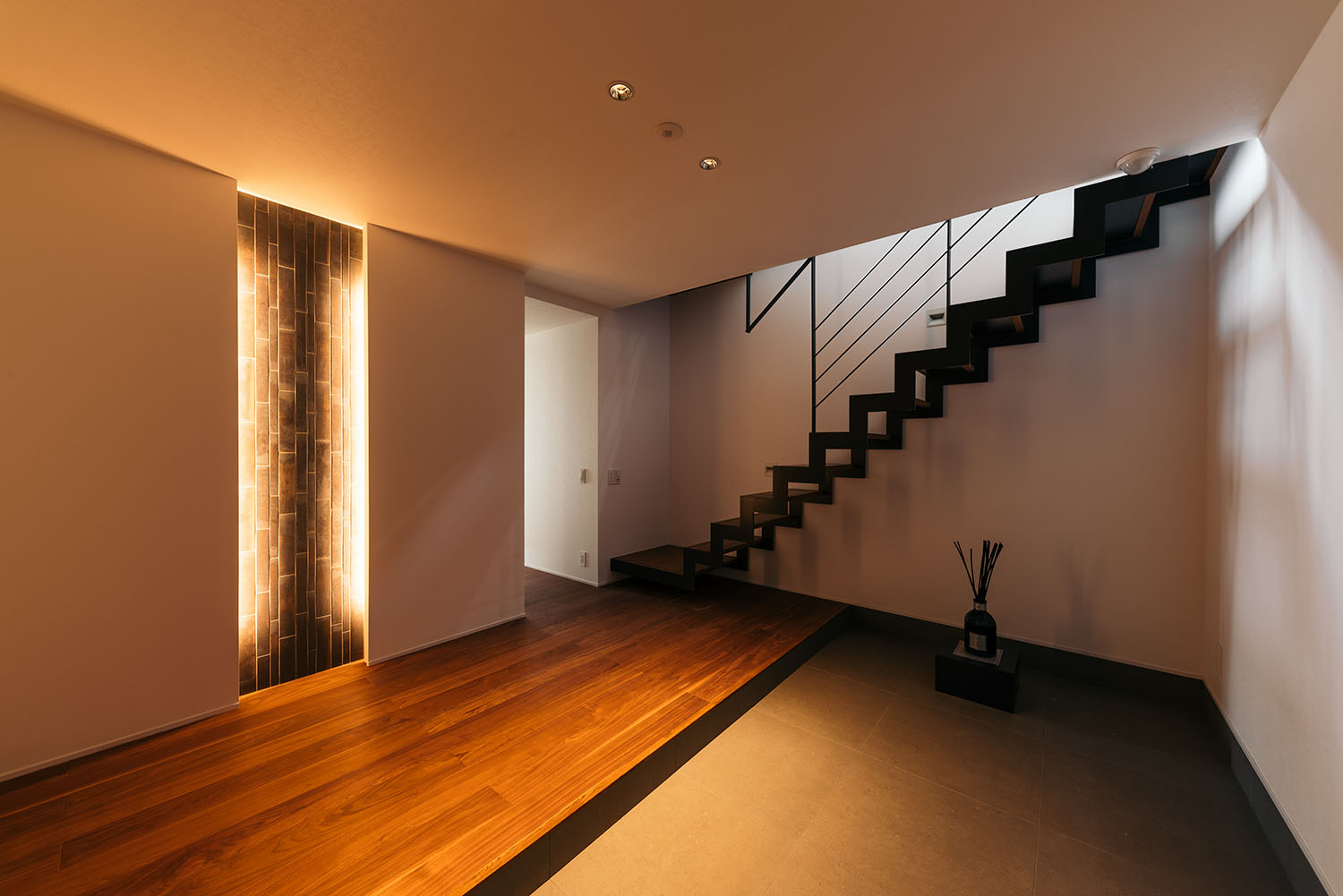 玄関に間接照明付きのアクセントウォールやアイアンのスケルトン階段がある様子・デザイン住宅 注文住宅・デザイン住宅建築実例_『CASE688 Transition』_玄関