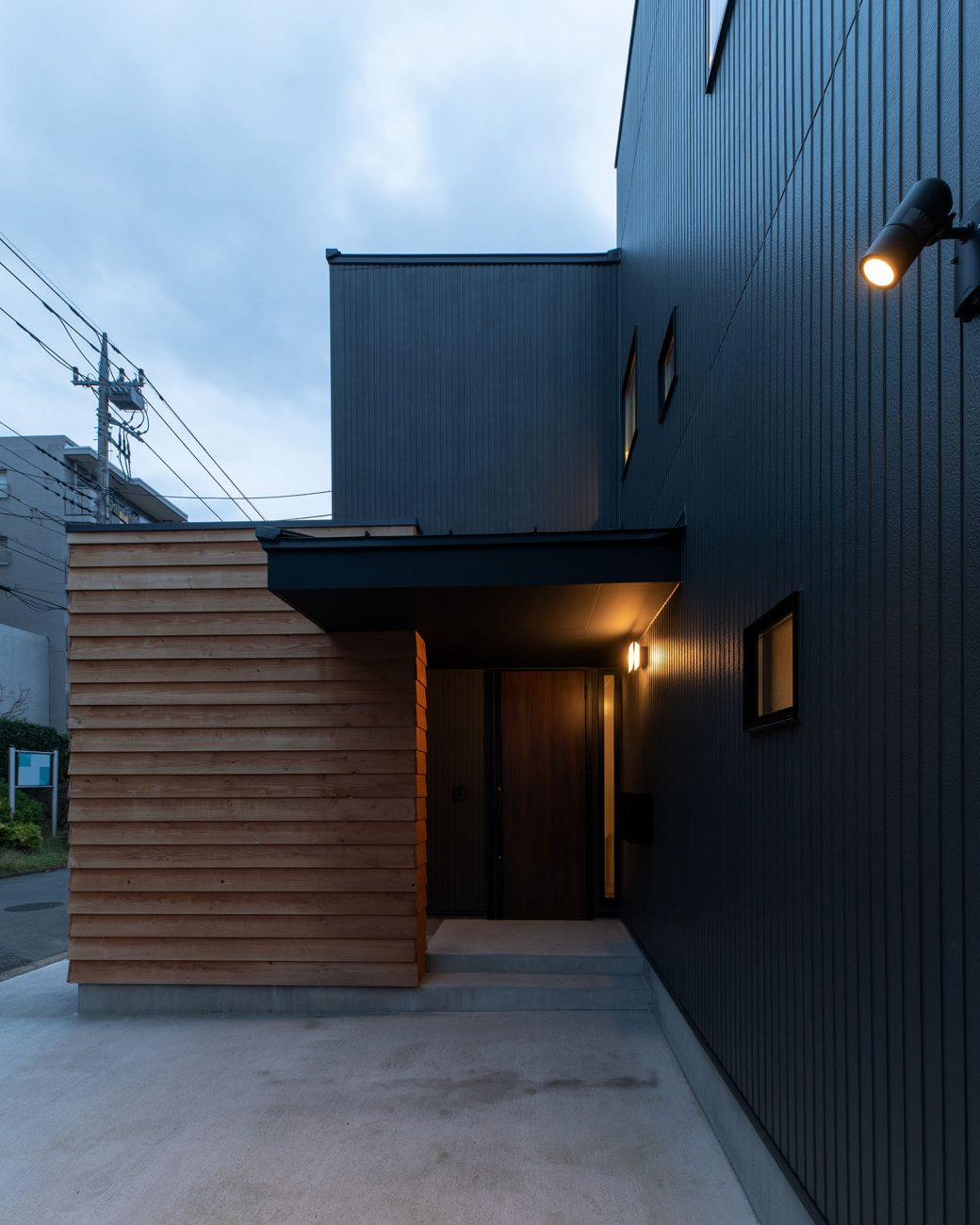 木材の壁が立てられた黒い外壁の住宅に屋外照明が取り付けられている・デザイン住宅 注文住宅・デザイン住宅建築実例_『CASE689 猫と寄り添う家』_外観
