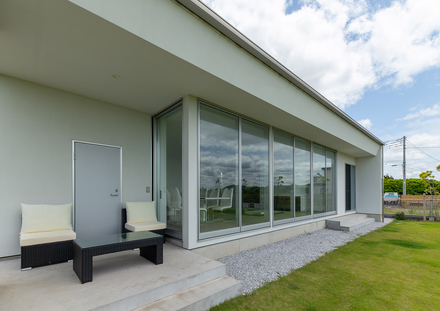 芝生の庭に面して大きな窓や、テーブルと椅子がある様子・デザイン住宅 注文住宅・デザイン住宅建築実例_『CASE750 WHITE　GATE』_外観