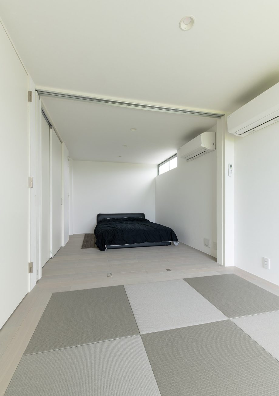 琉球畳を敷いた和室と黒いベッドのある寝室が引き戸で仕切られている様子・デザイン住宅 注文住宅・デザイン住宅建築実例_『CASE750 WHITE　GATE』_和室