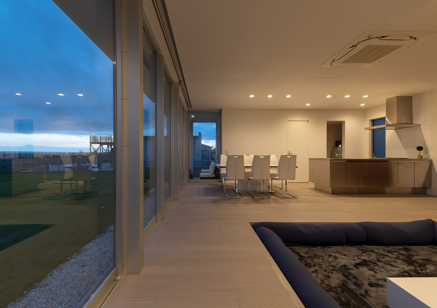 ダウンライトによって照らされたLDKから芝生の庭が見える様子・デザイン住宅 注文住宅・デザイン住宅建築実例_『CASE750 WHITE　GATE』_LDK