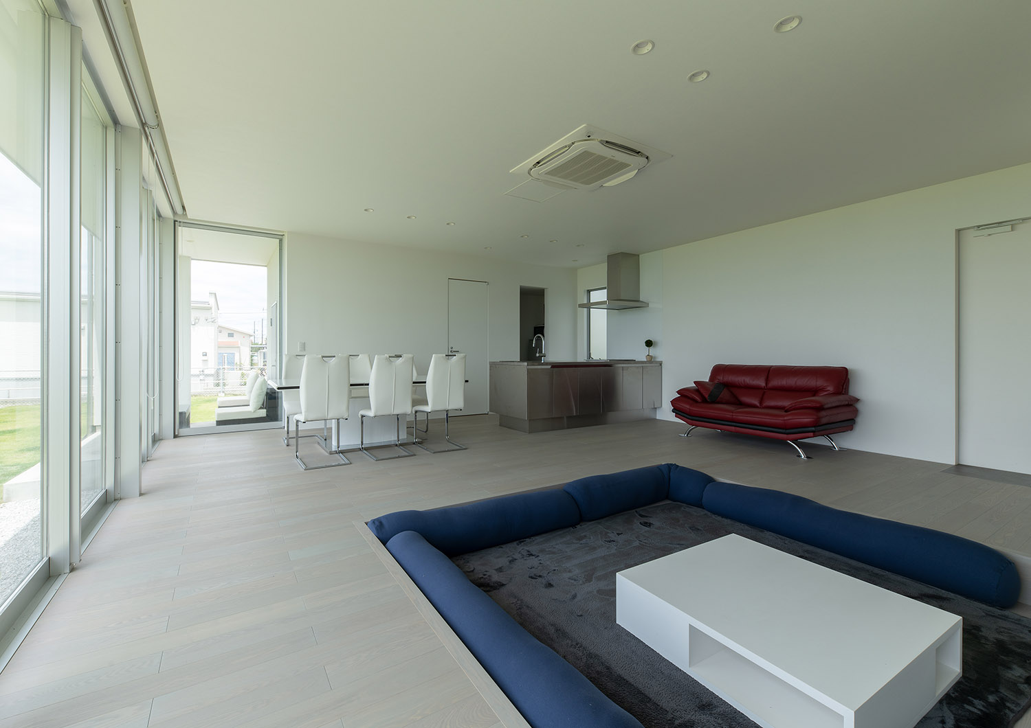 青いクッションがあるダウンリビングからキッチンやダイニングテーブルを見た様子・デザイン住宅 注文住宅・デザイン住宅建築実例_『CASE750 WHITE　GATE』_LDK