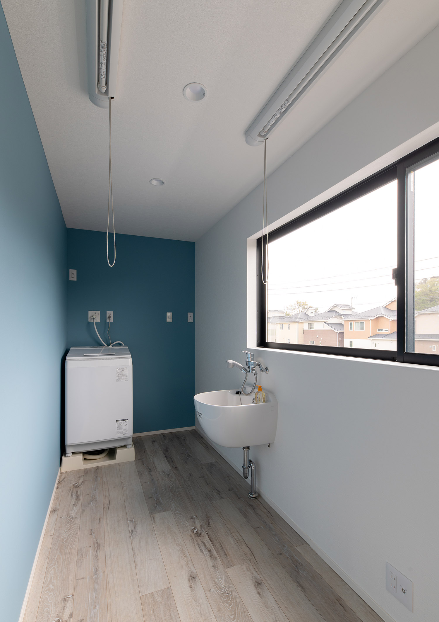青い壁で、室内干しが出来る物干し竿があるランドリールーム・デザイン住宅 注文住宅・デザイン住宅建築実例_『CASE751 Contarst』_浴室・洗面所
