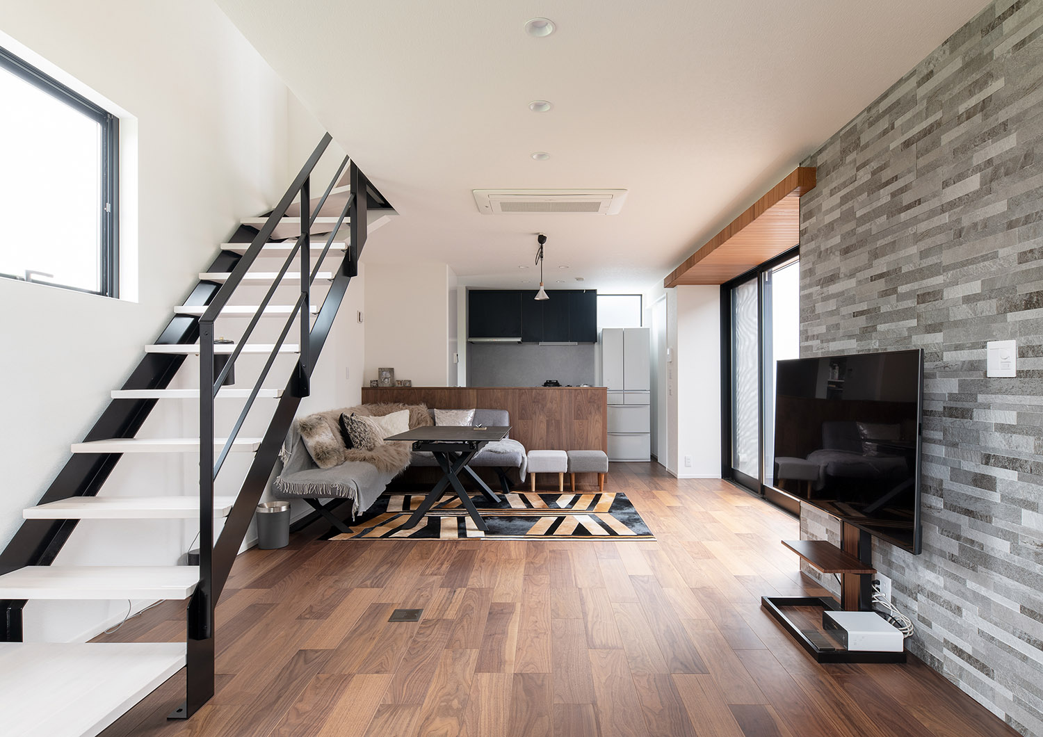 グレーのアクセントウォールの前にテレビが置かれた、白いスケルトン階段のあるLDK・デザイン住宅 注文住宅・デザイン住宅建築実例_『CASE751 Contarst』_LDK