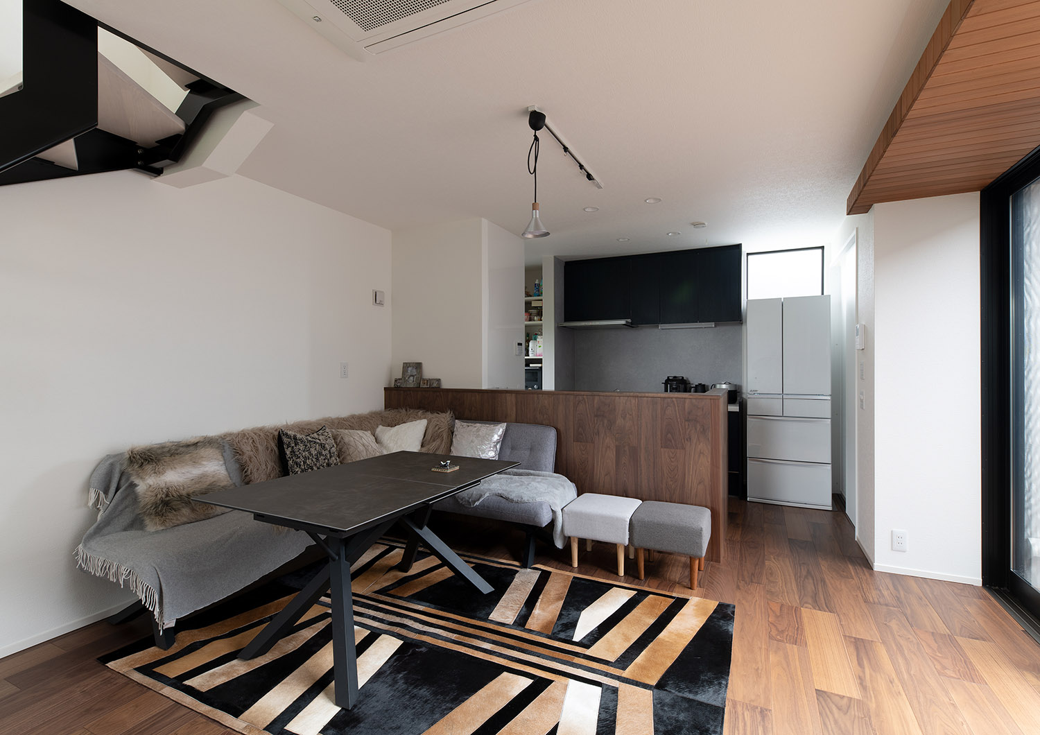 腰壁付きのキッチンの前にL字ソファーが置かれたマットの敷かれたLDK・デザイン住宅 注文住宅・デザイン住宅建築実例_『CASE751 Contarst』_LDK