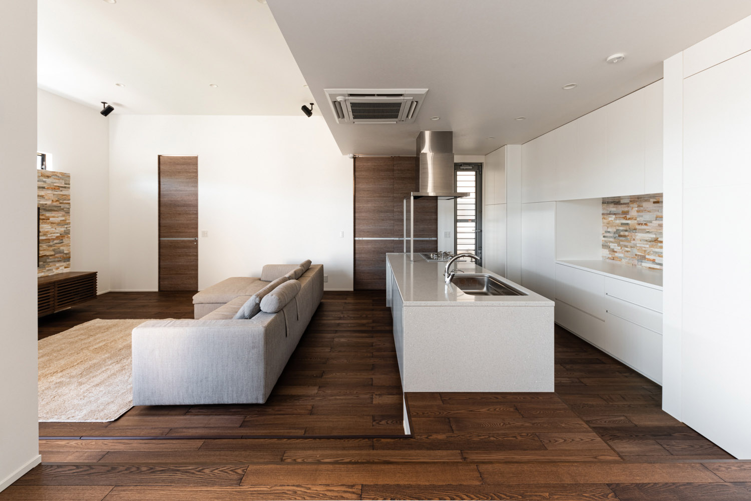 白いキッチンの前にグレーのL字ソファーがあるフローリングのLDK・デザイン住宅 注文住宅・デザイン住宅建築実例_『CASE754 首途(かどで)の家』_LDK