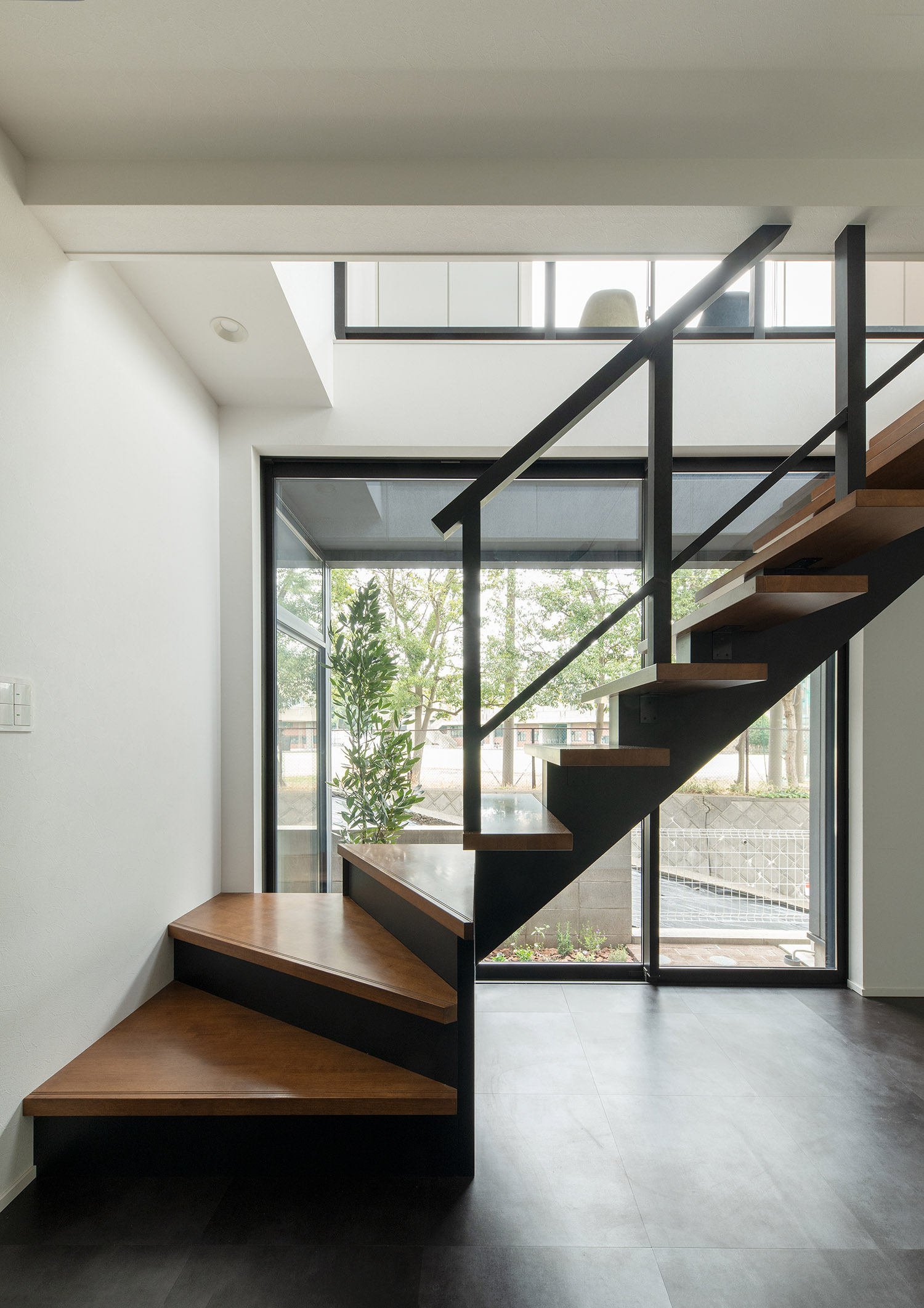 そばに大きな窓が設けられた木製で黒の手すりのスケルトン階段・デザイン住宅 注文住宅・デザイン住宅建築実例_『CASE755 山際の家（やまぎわのいえ）』_階段
