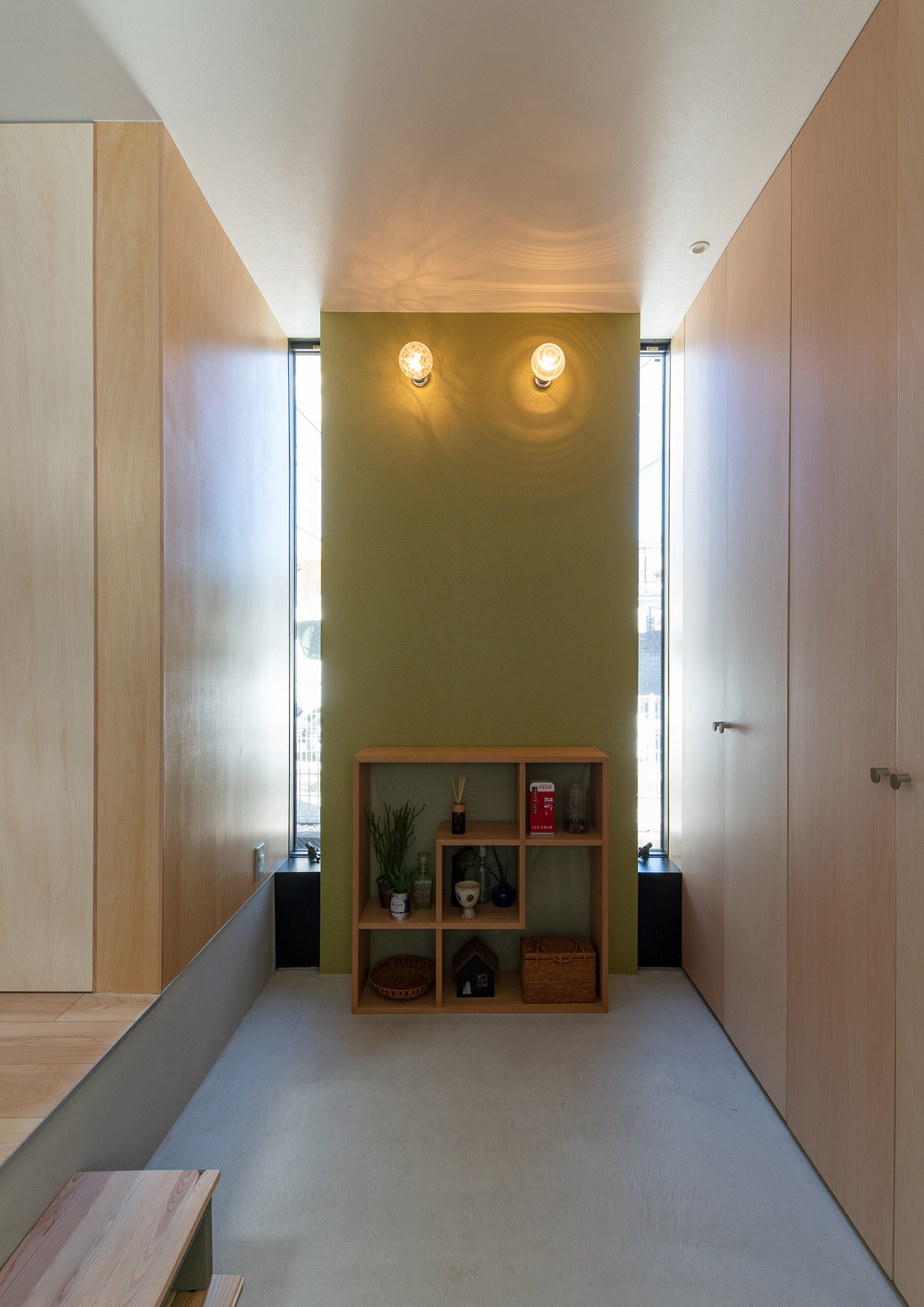 グリーンのアクセントウォールに照明を取り付けた明るいモルタルの玄関・デザイン住宅 注文住宅・デザイン住宅建築実例_『CASE761 光と明かりの交錯』_玄関