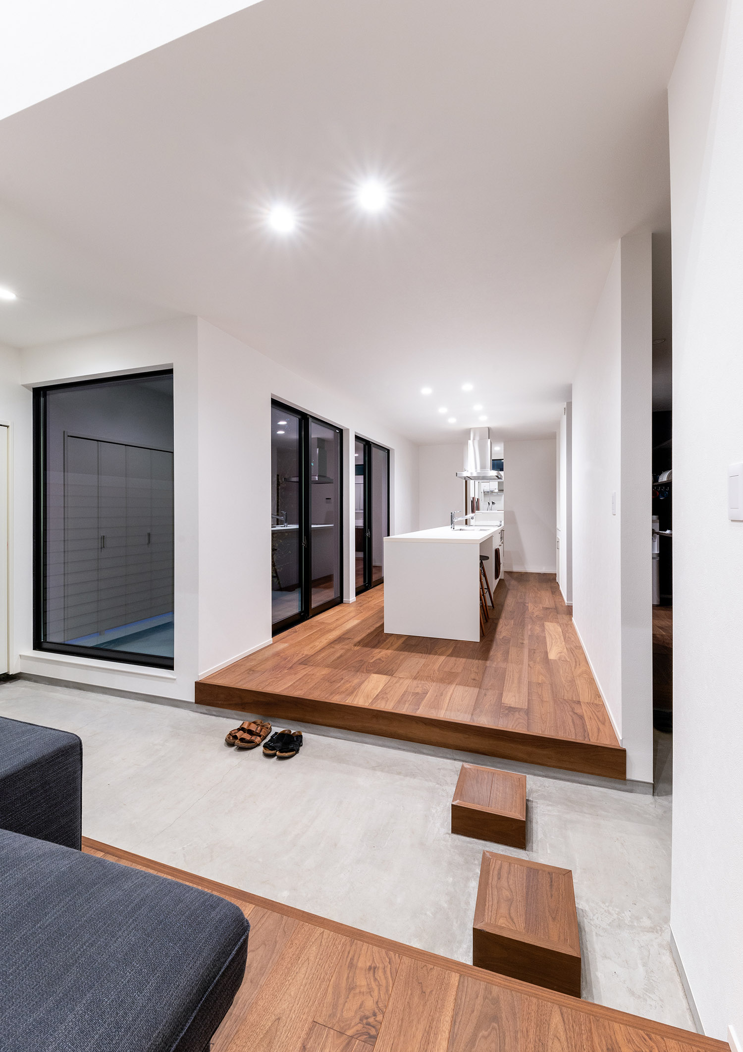 土間玄関越しに白いキッチンがあるLDKを見た様子・デザイン住宅 注文住宅・デザイン住宅建築実例_『CASE763 ソト黒ウチ白』_LDK